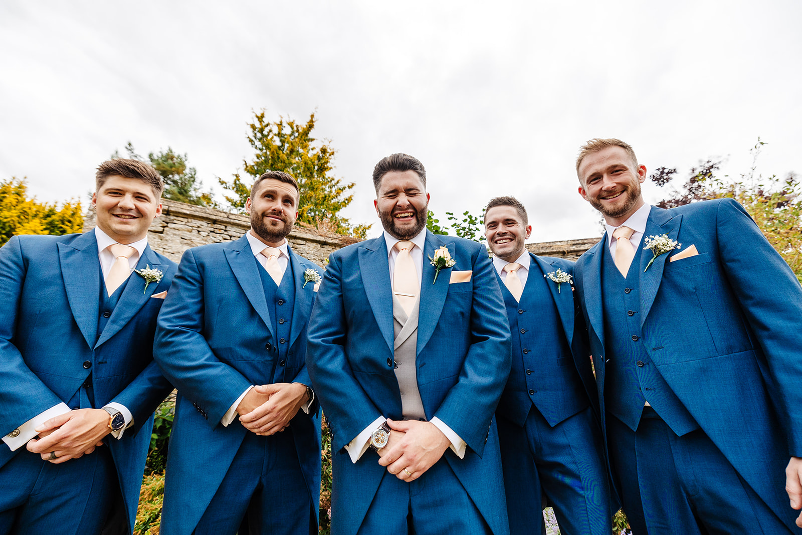 Groomsmen with groom in the centre in blue suits with champagne coloured ties outside Caswell House