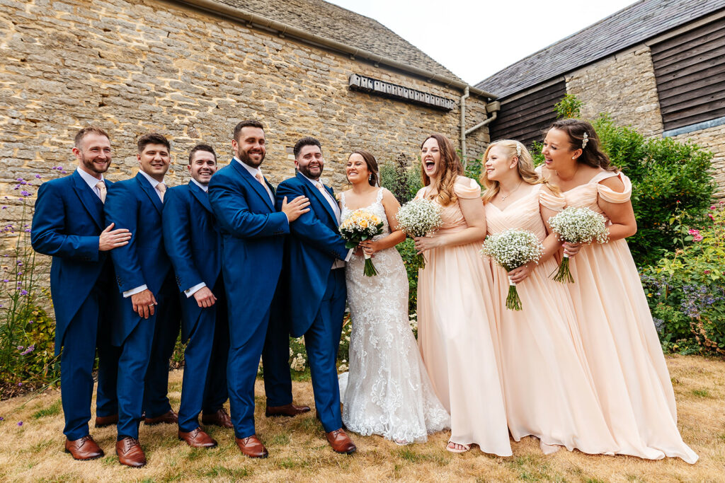 Bridal party and Groomsmen with couple in the centre, groomsmen are in blue suits and bridesmaids are in pastel peach dresses holding bunches of gypsophelia 