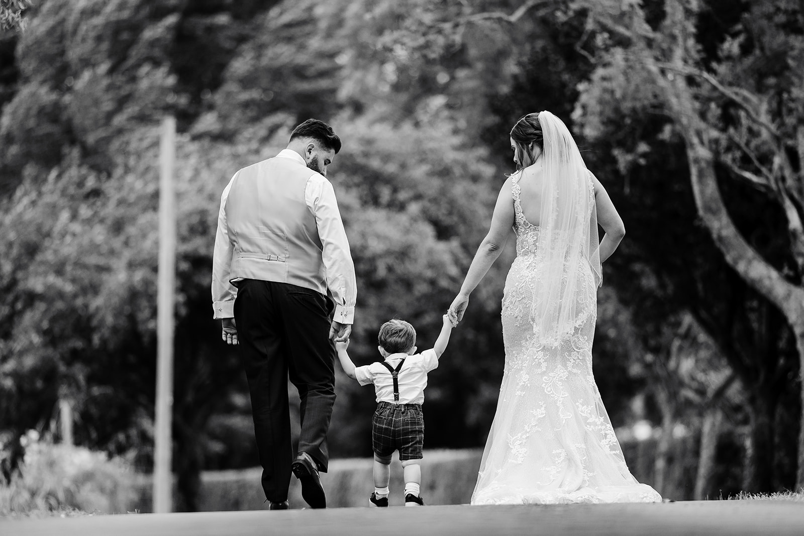 Couple take a walk through grounds of Caswell House with their son between them holding hands, in black and white 