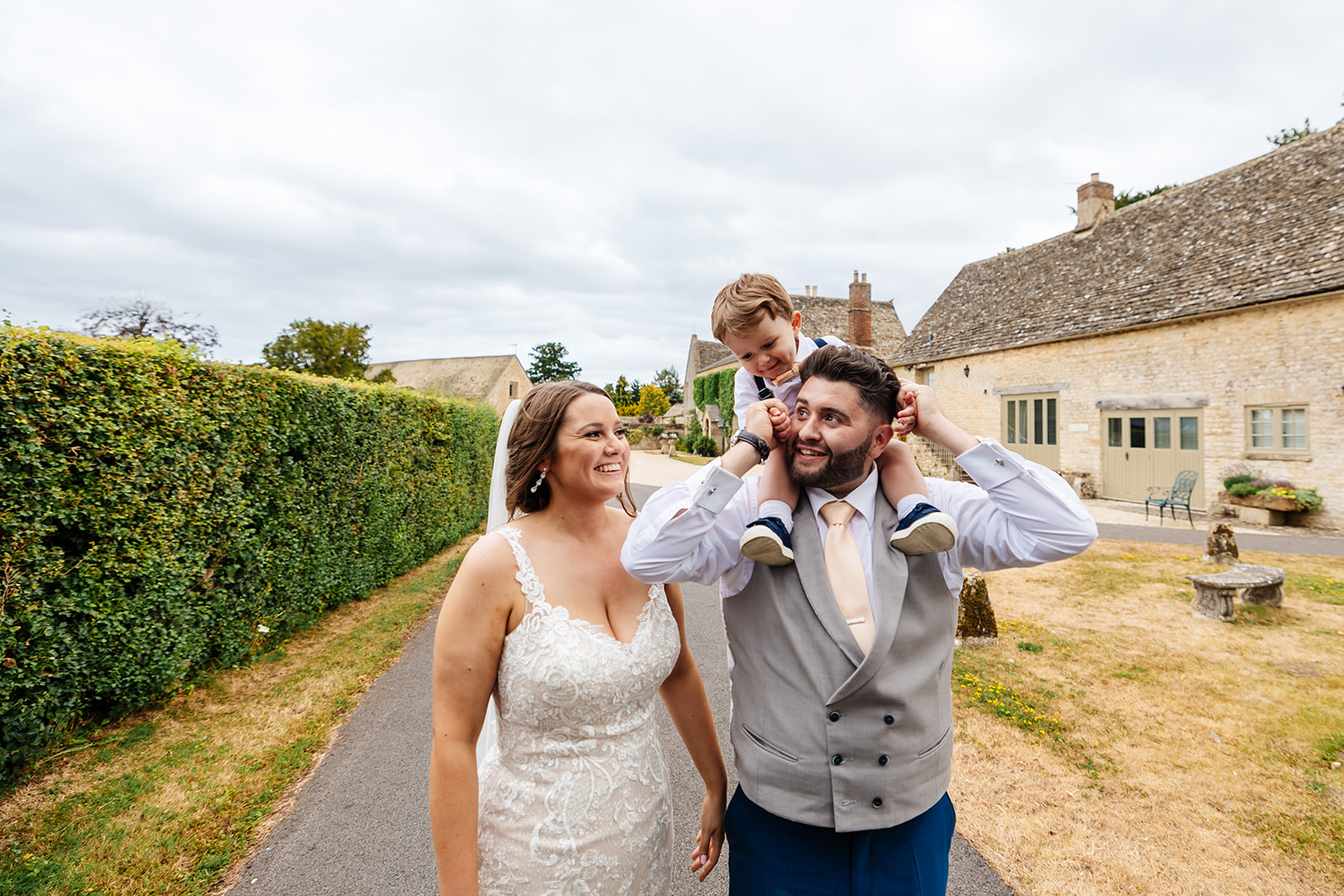 Couple take a walk through grounds of Caswell House with their son on the grooms shoulders smiling 