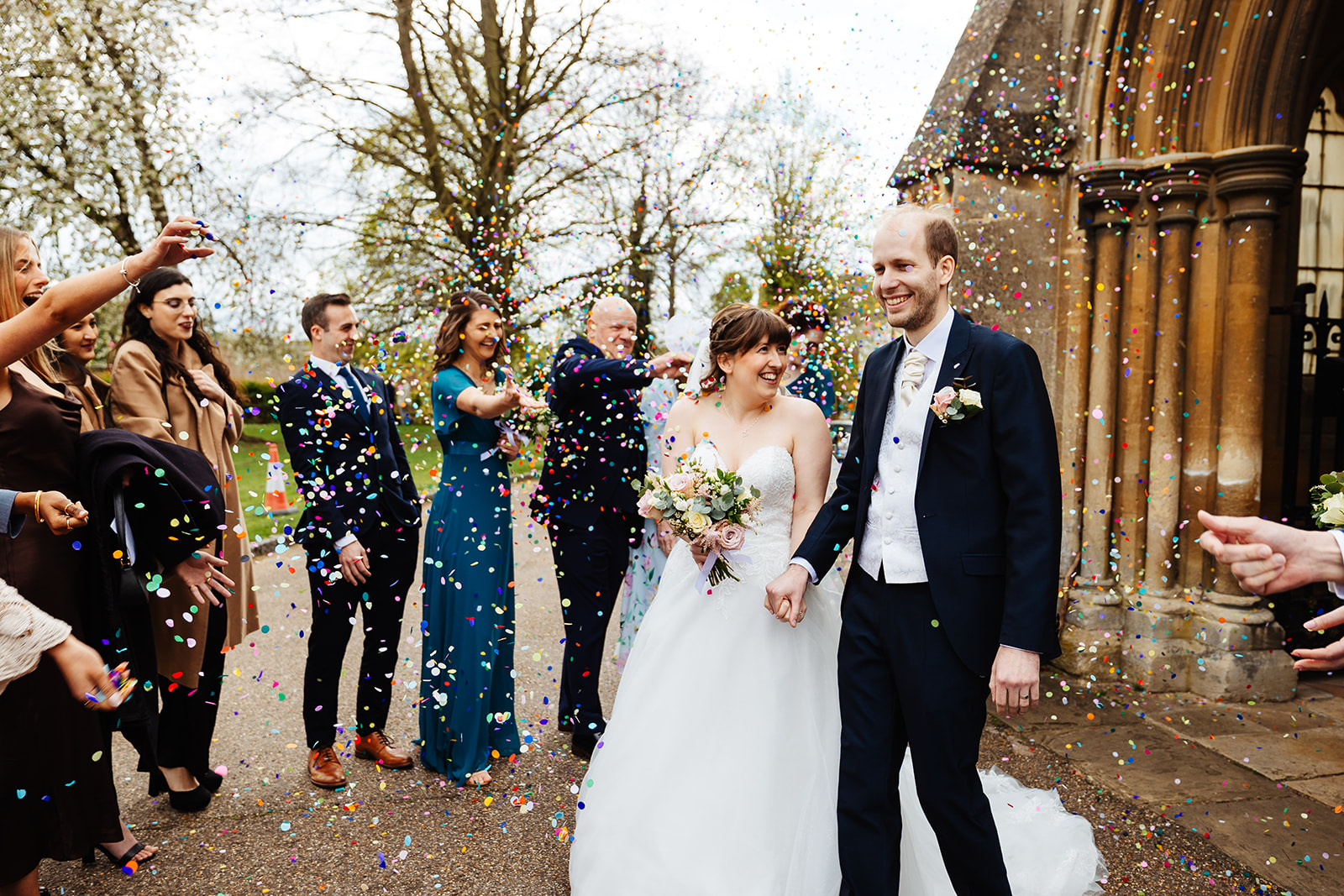 A newly married couple outside the church with guests throwing confetti over them