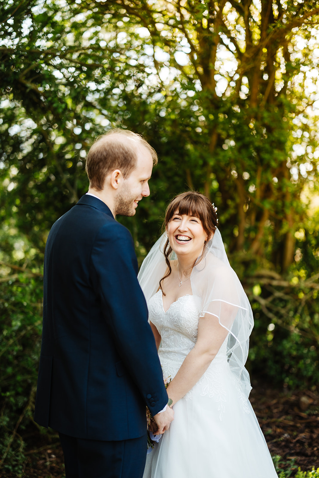 bride and groom stood together smiling amidst greenery 