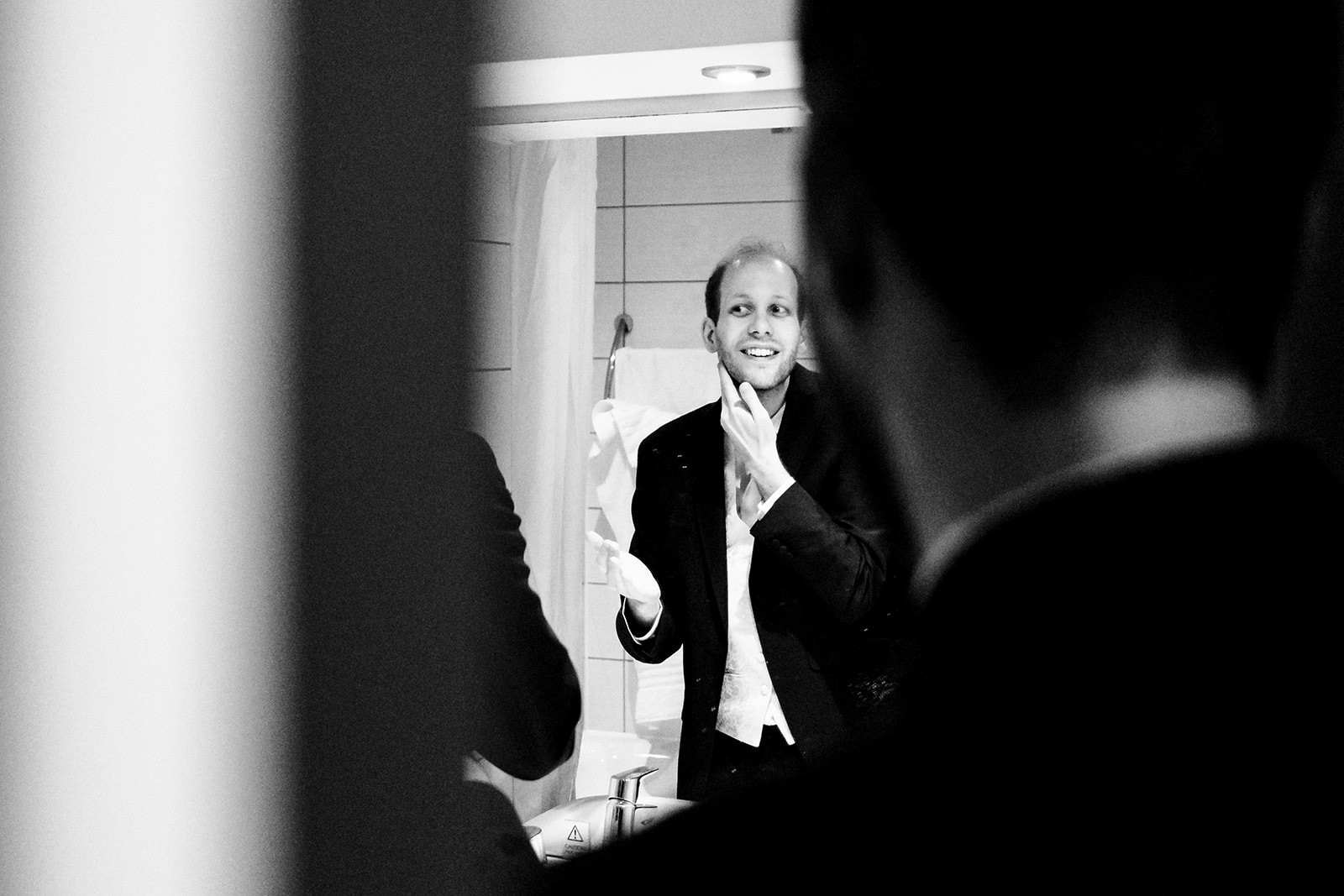 A groom getting ready by putting on aftershave with his hand on his neck. The photo is black and white