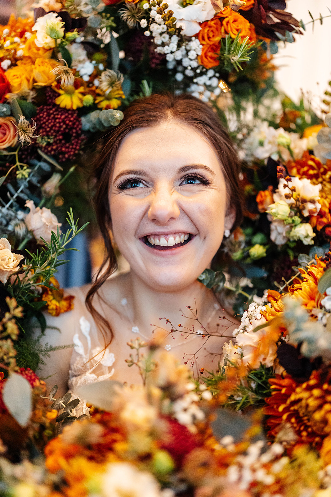 The brides face in the middle of a gorgeous bunch of orange and yellow flowers. The bride is smiling