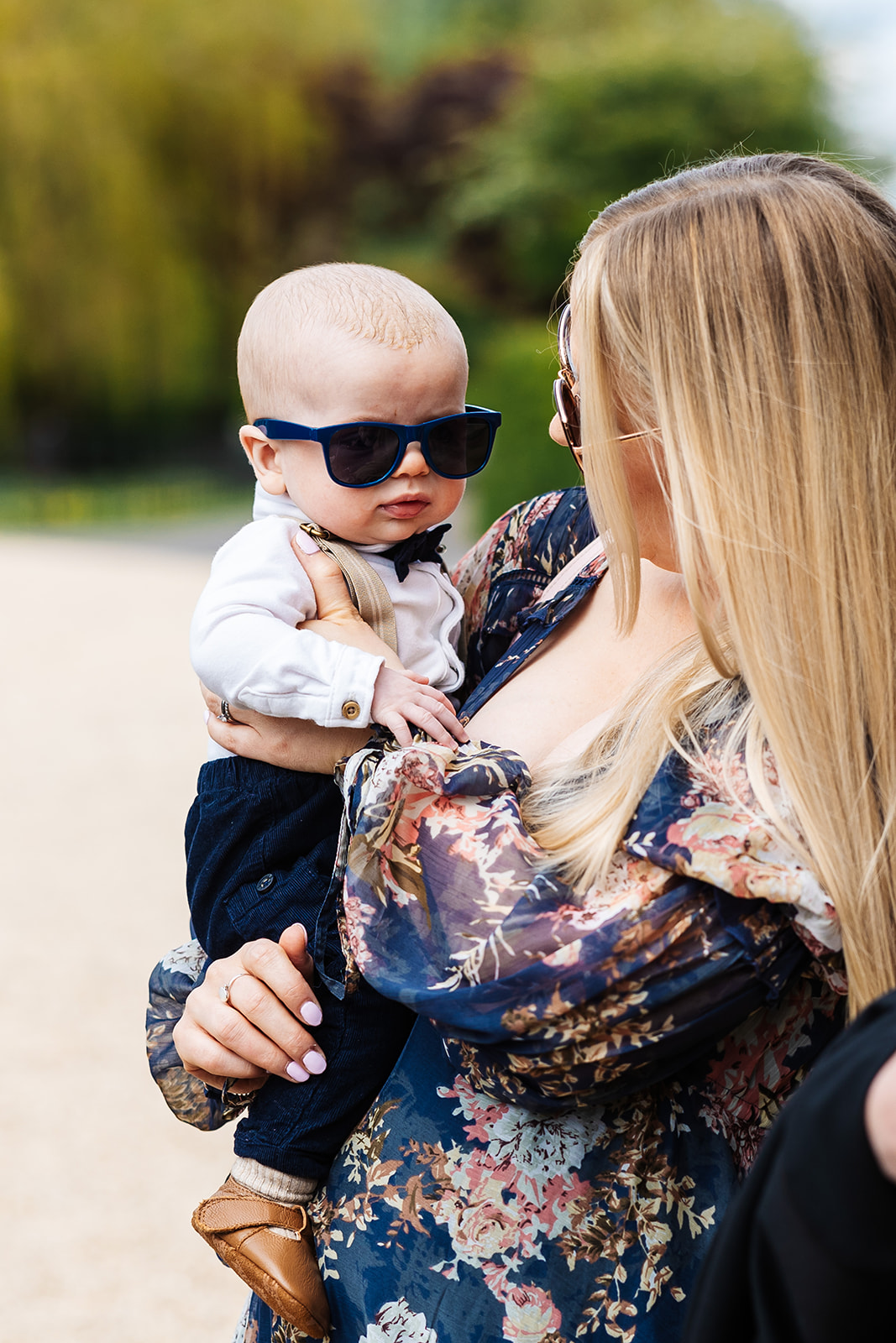 A blonde woman holding a baby who is wearing a bow tie and sunglasses