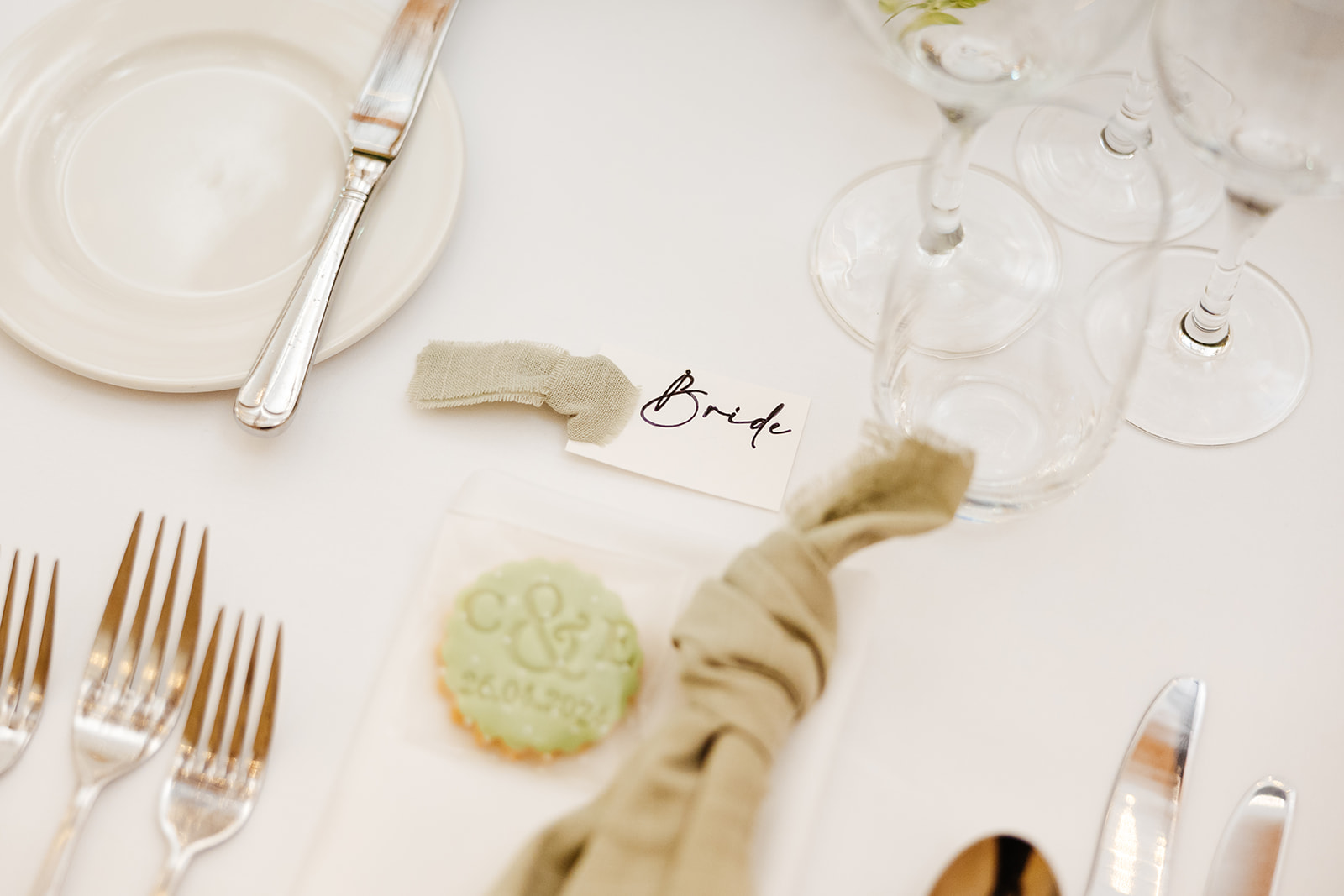 A white table cloth at a wedding with a luggage tag with Bride written on it and a personalised cookie with the date of the couple's wedding day and their initials embossed into it