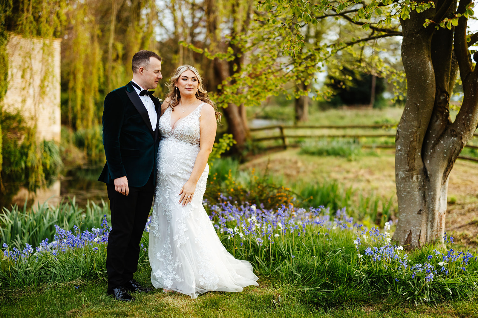 A newlywed couple standing in a garden of bluebells and white flowers smiling after they have got married
