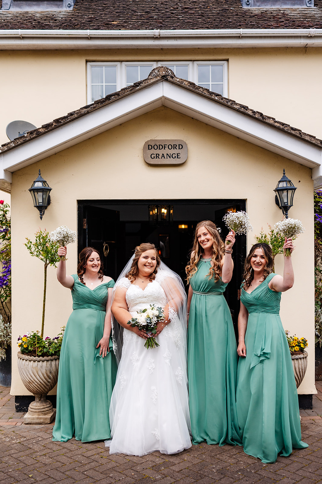 A bride in a white dress and her bridesmaids in a soft mint coloured dress infront of a doorway holding flowers