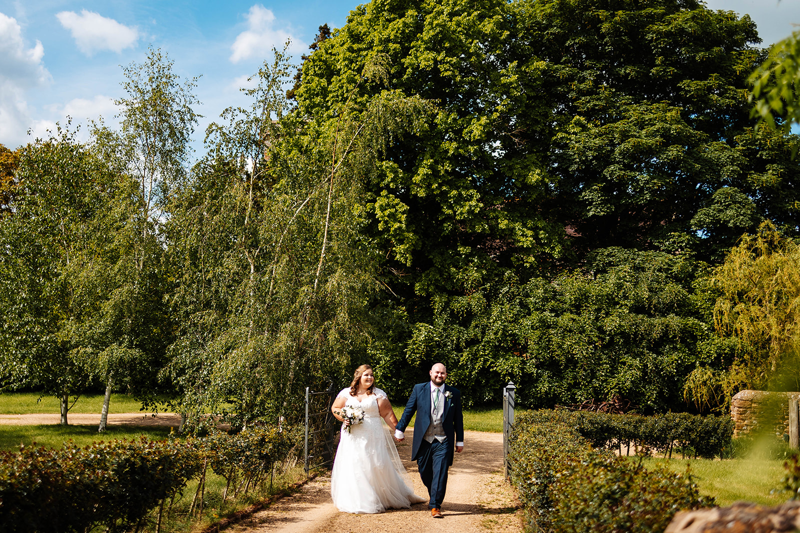 A bride and groom holding hands outside in a green garden