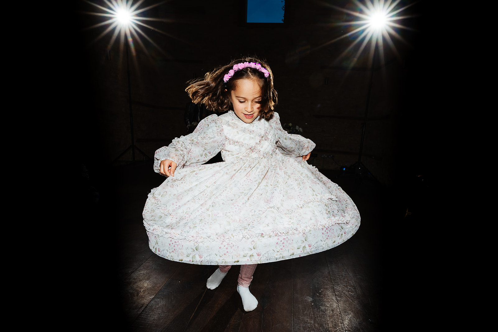 A little girl twirling on the dance floor and her white dress is floating in the air