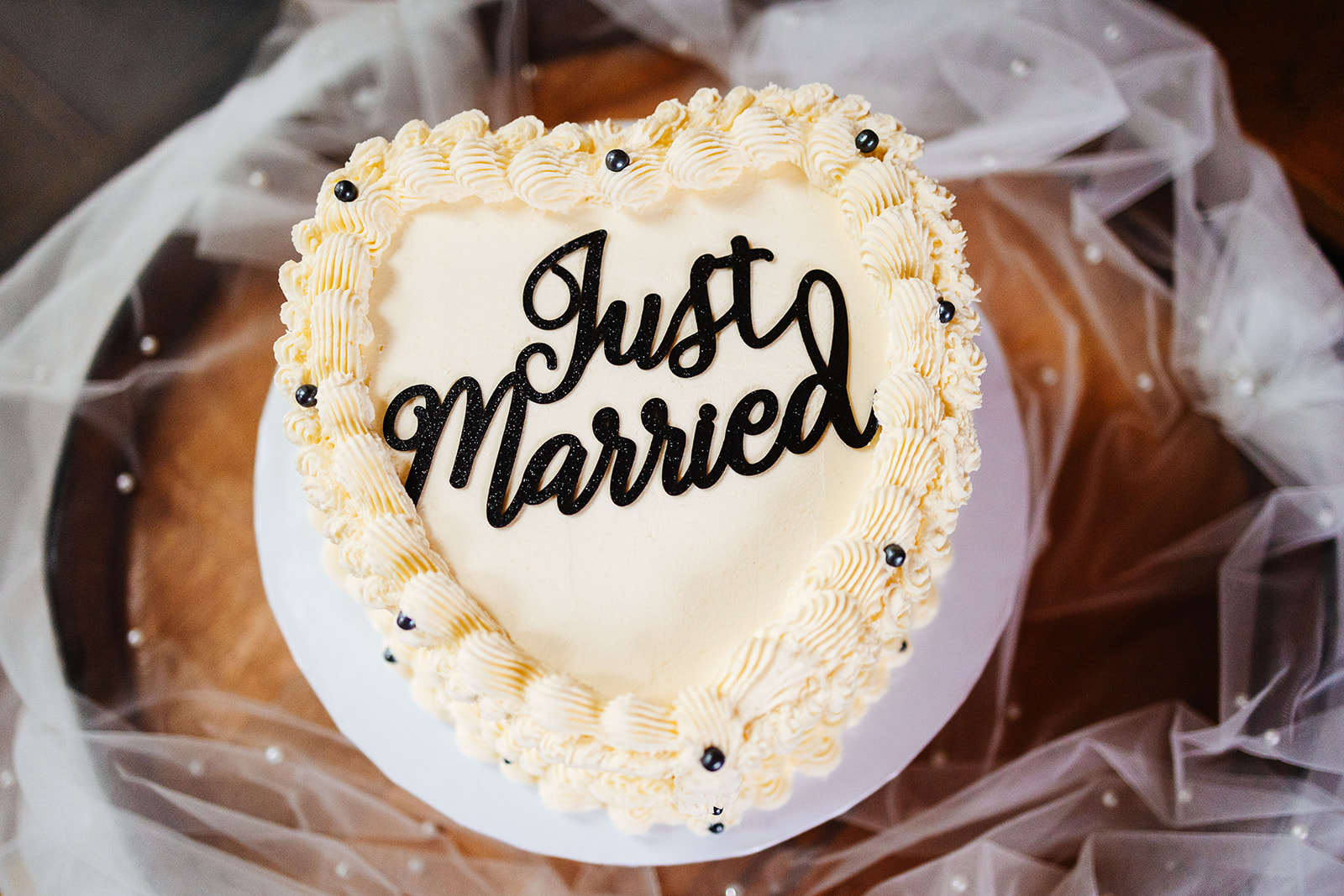 A cream white heart wedding cake with Just Married written in black curved writing on the top