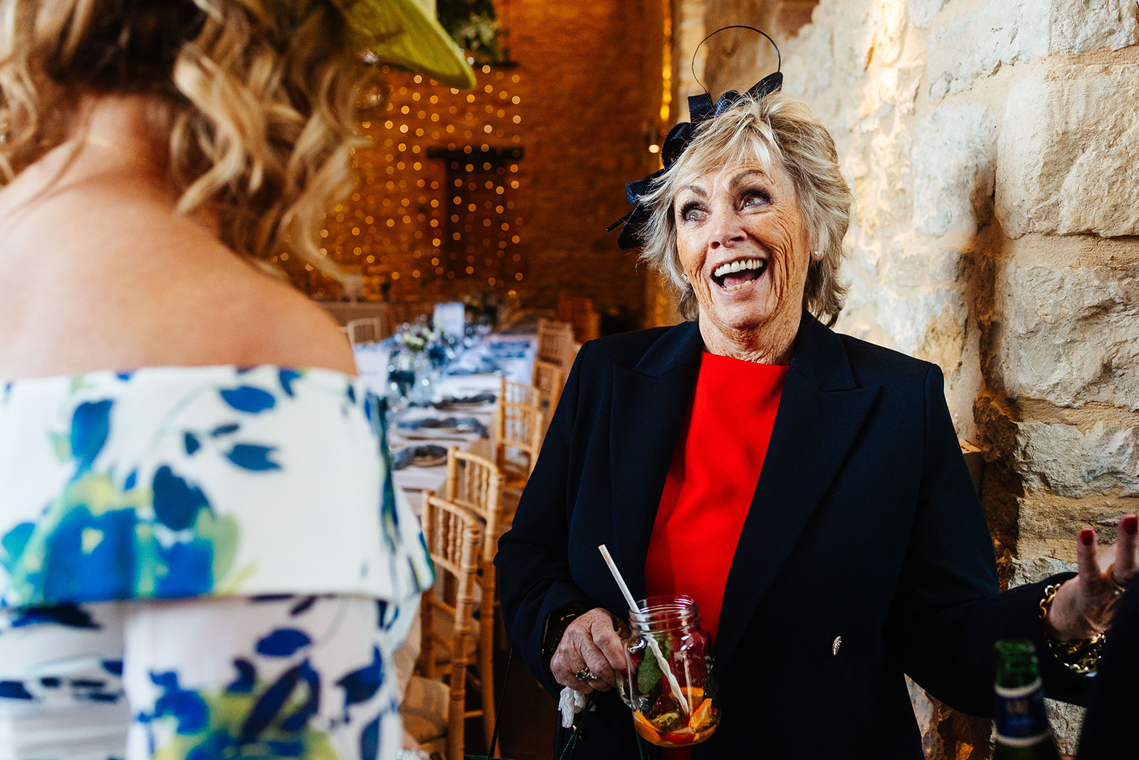 A wedding guest in a red dress and black blazer smiling and enjoying herself