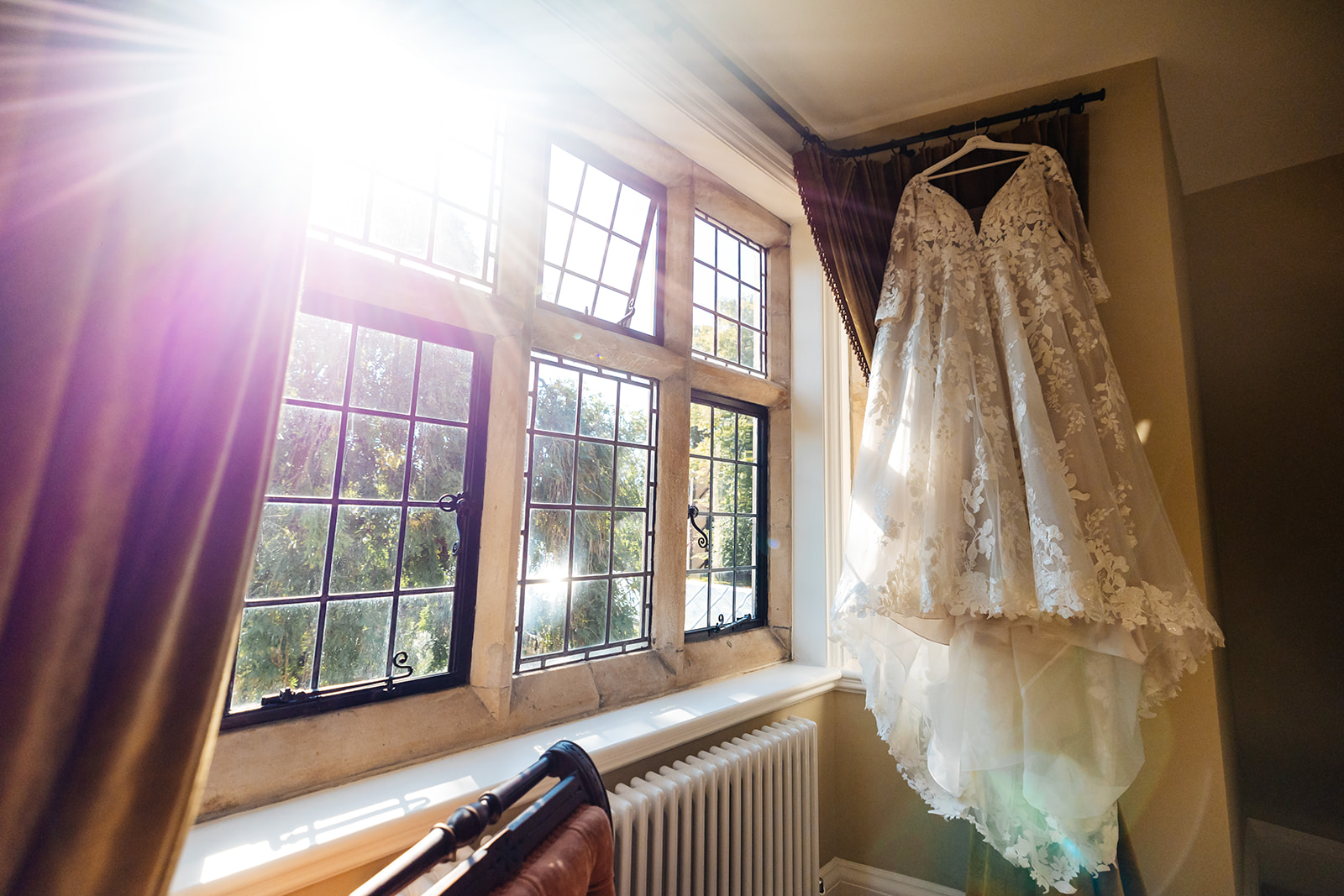 A long, white wedding dress hanging up with the sunlight pouring in the window
