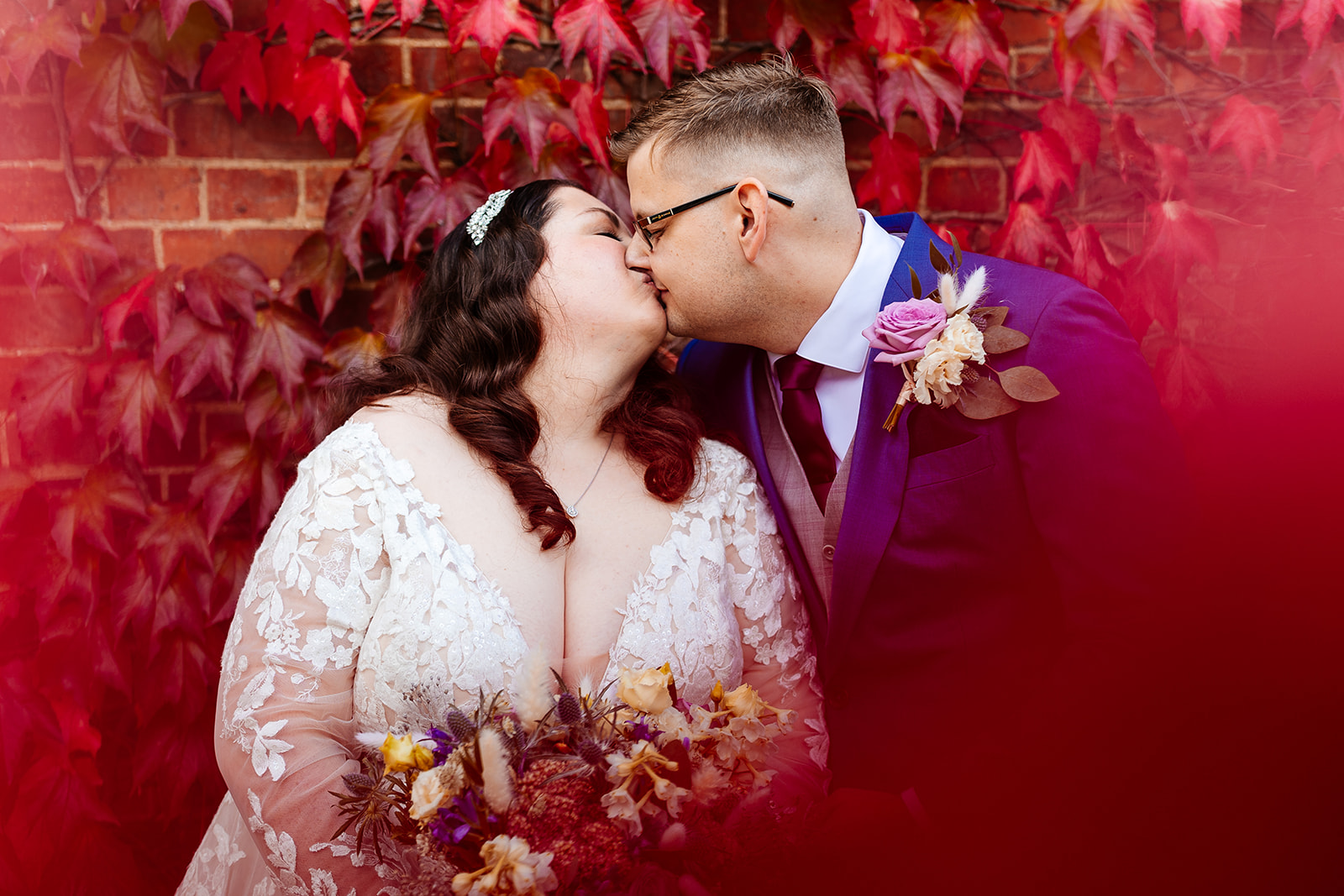 A newly married couple kissing on their wedding day infant of red, autumnal leaves