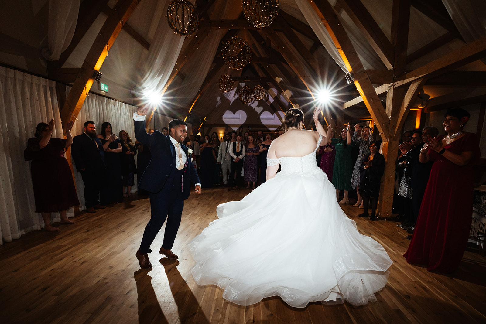 A married couple in a wooden barn during their first dance with their hands in the air enjoying themselves
