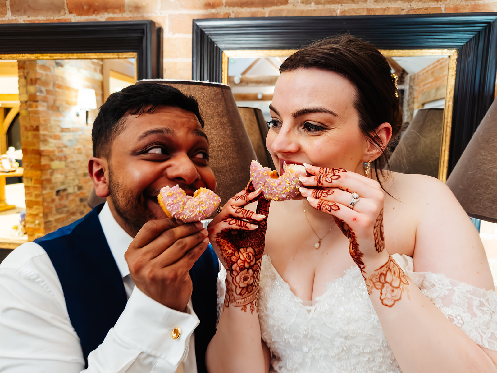 A newly married couple eating a doughnut in the shape of a smile whilst looking at each other lovingly