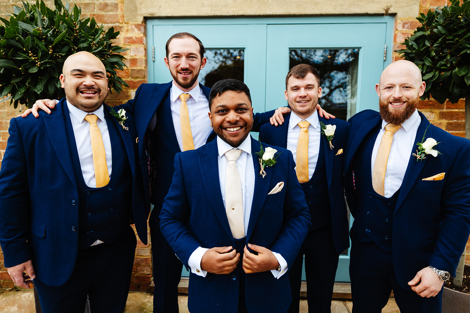 A groom and his groomsman stood outside a duck egg blue door in their navy blue suits