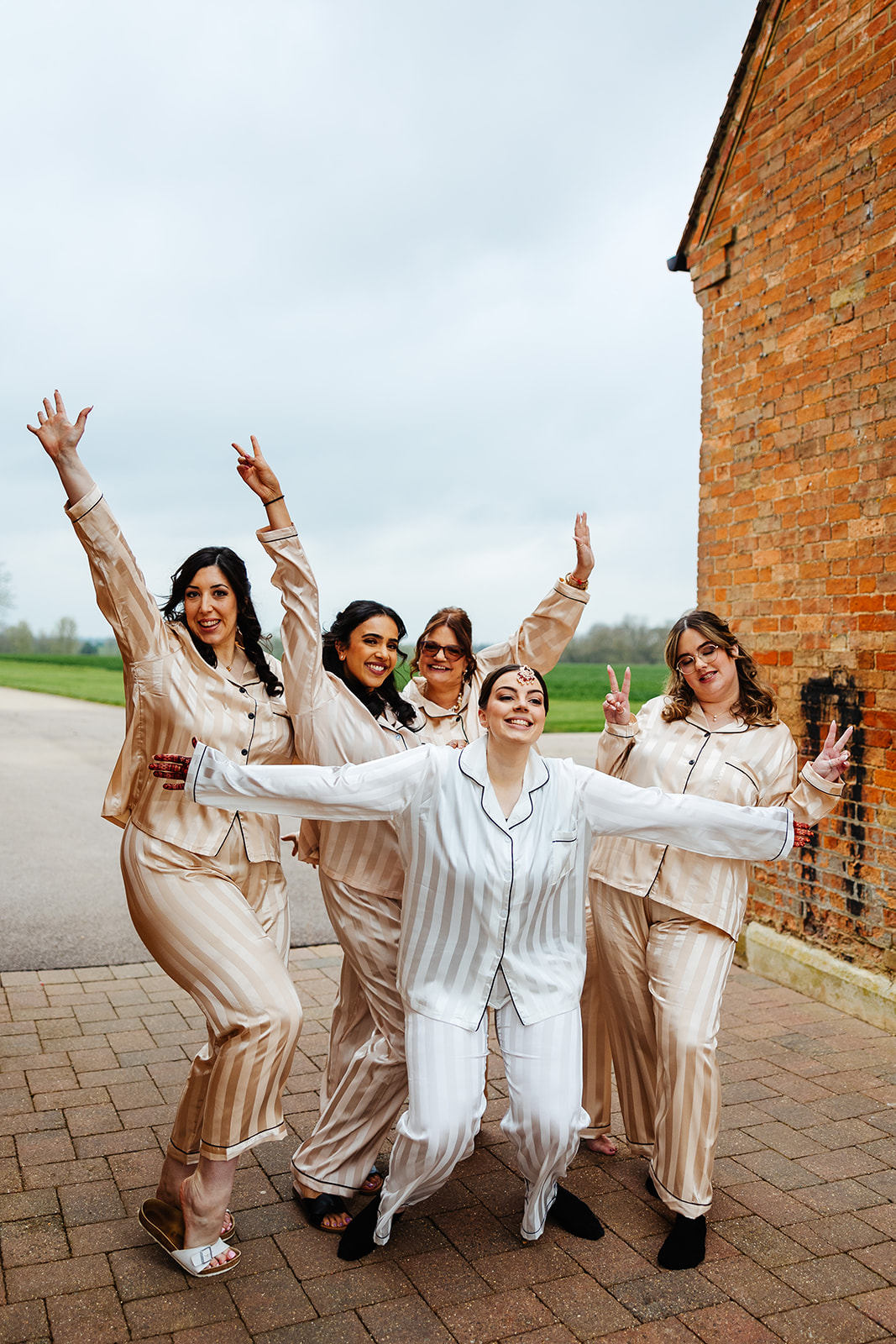 A bride in silky white striped pajamas and her bridemaids in cream silky pajamas. They are pulling funny faces and poses having lots of fun.