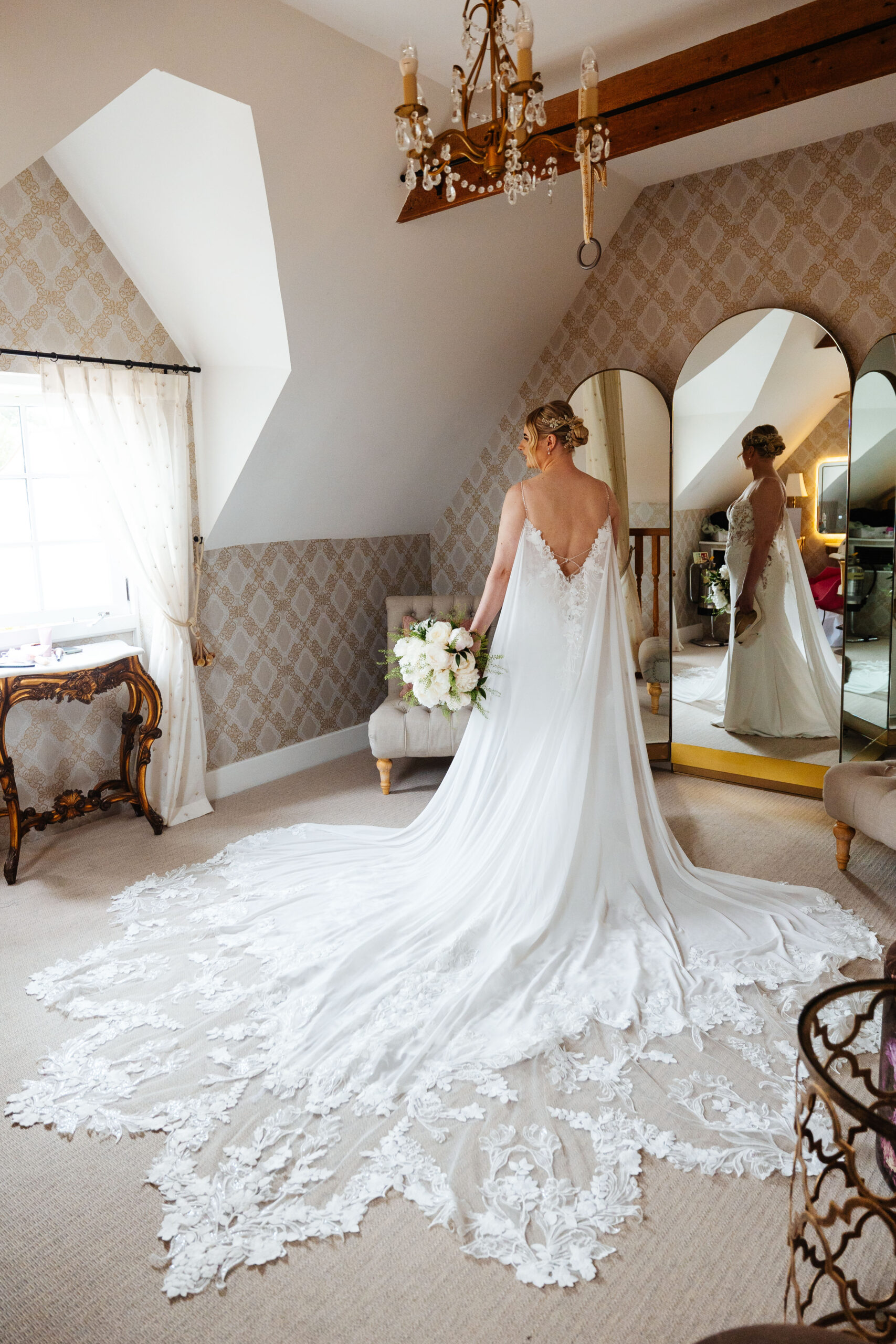 A bride getting ready in her dress. The dress has a very long train to it and has laced detail at the bottom.