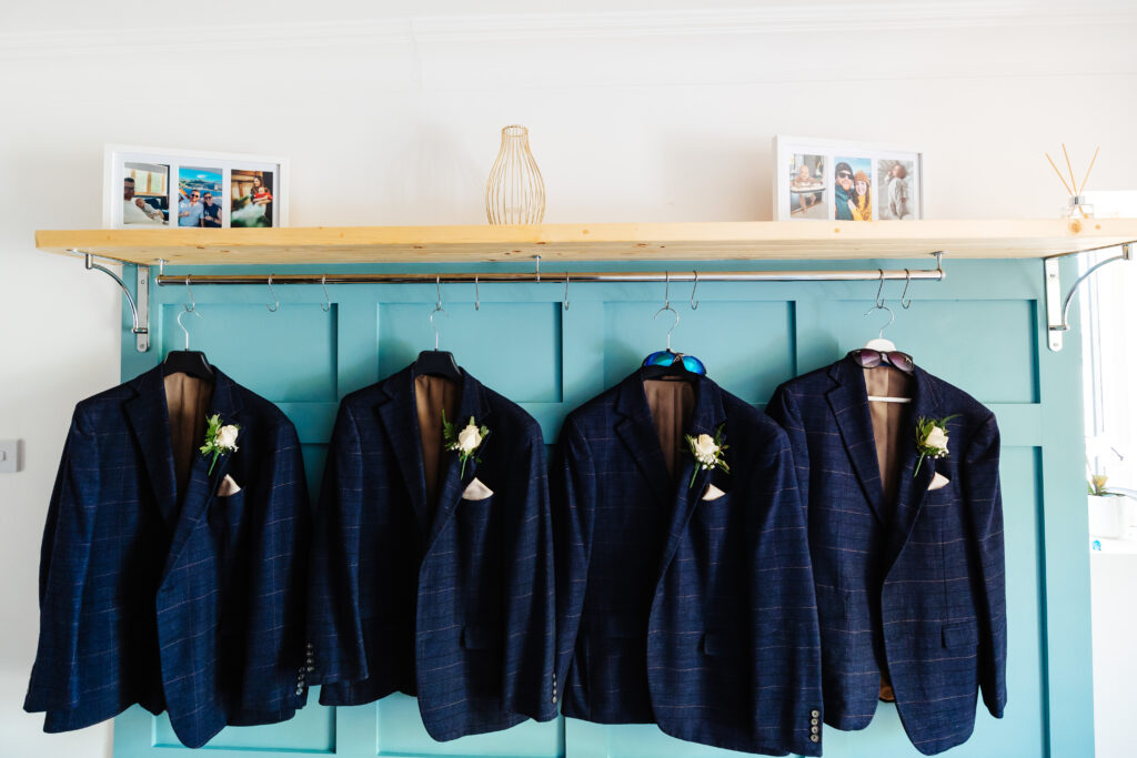 Four navy blue striped blazers hung up with a wooden background.