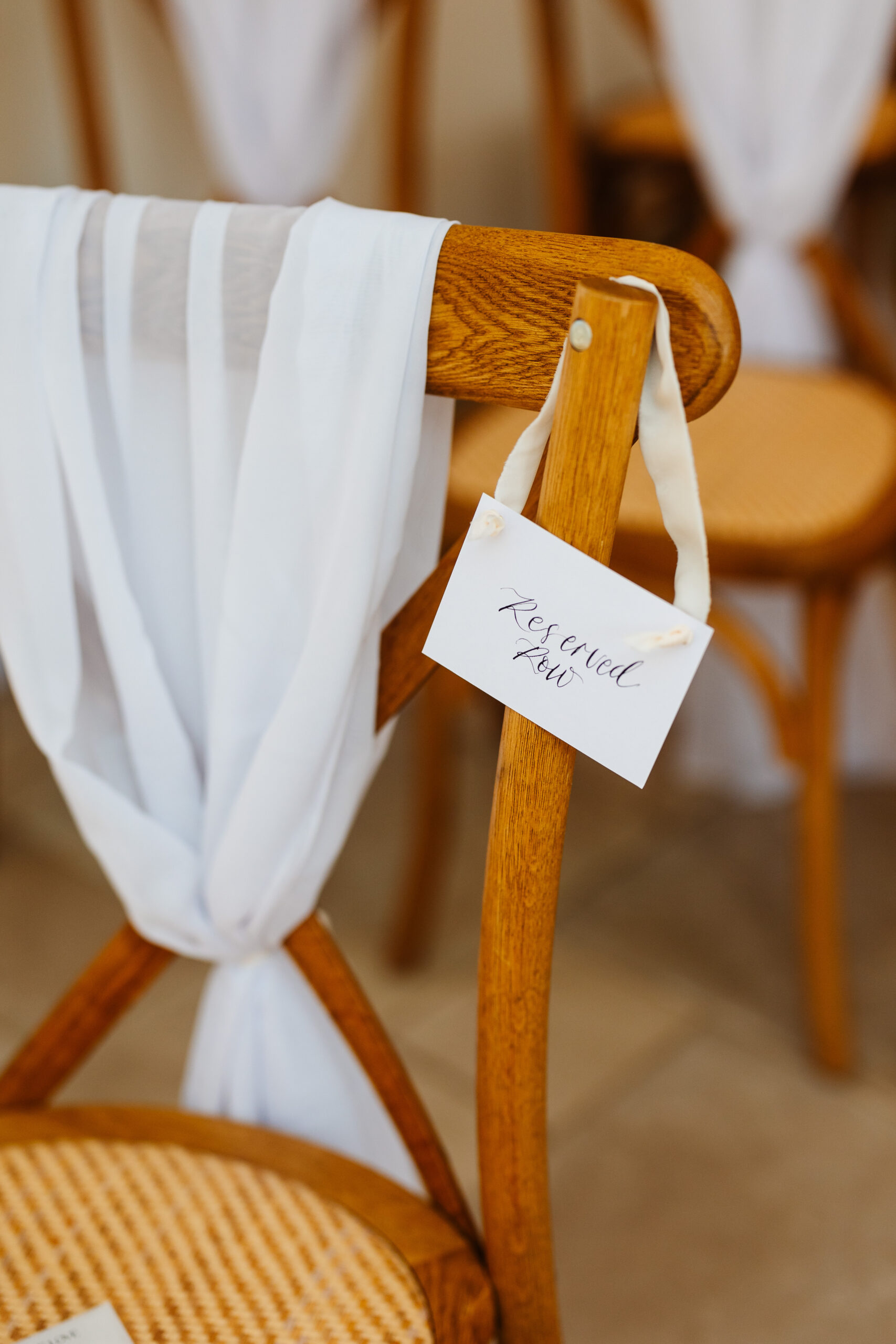 A wooden chair with a white drape over it and a sign hanging from it saying "reserved row" in calligraphy lettering.