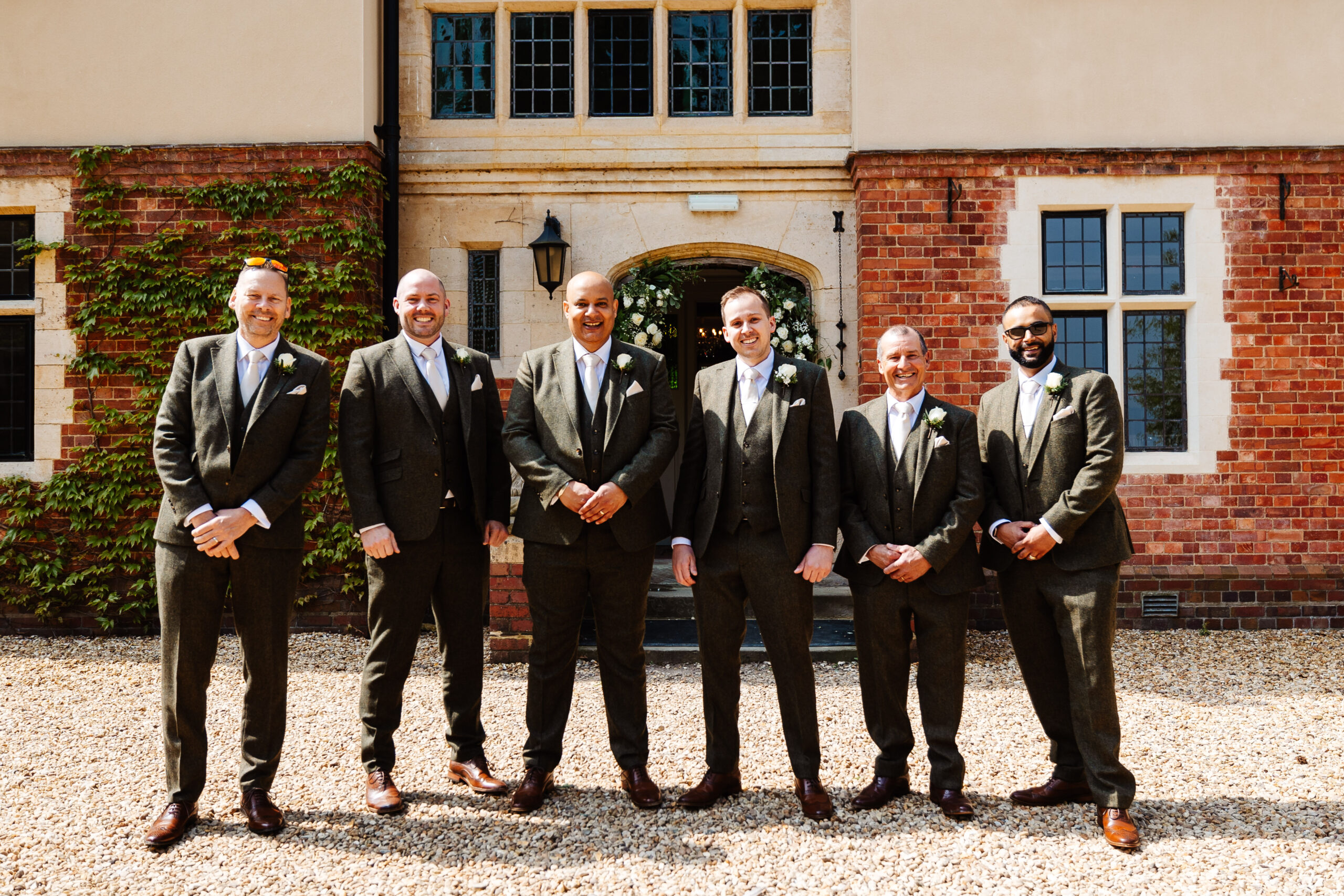 A group of men dressed in dark green tweed suits looking relaxed and smiling at the camera.