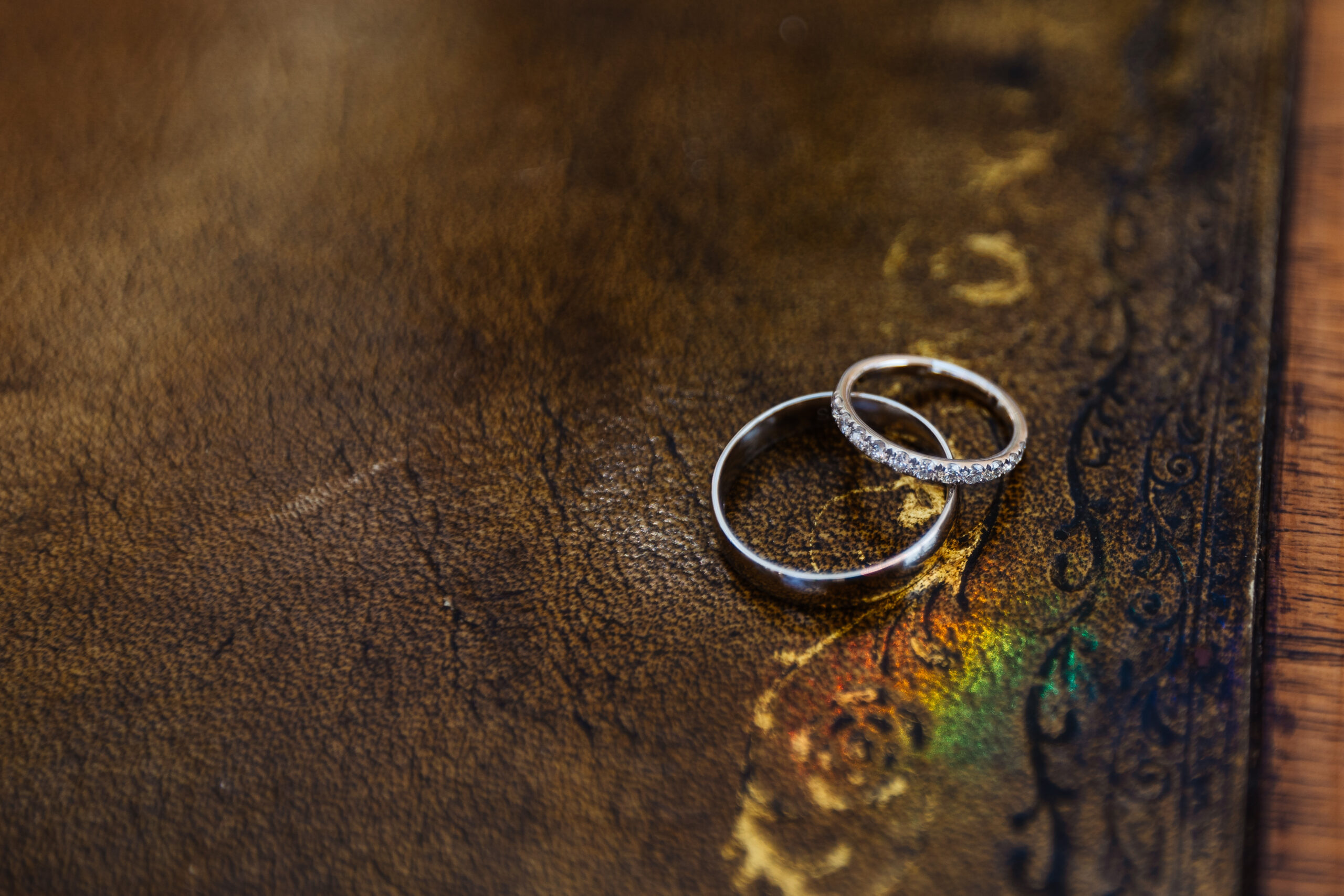 A pair of silver wedding rings on a leather background. One of them has diamonds around the band.