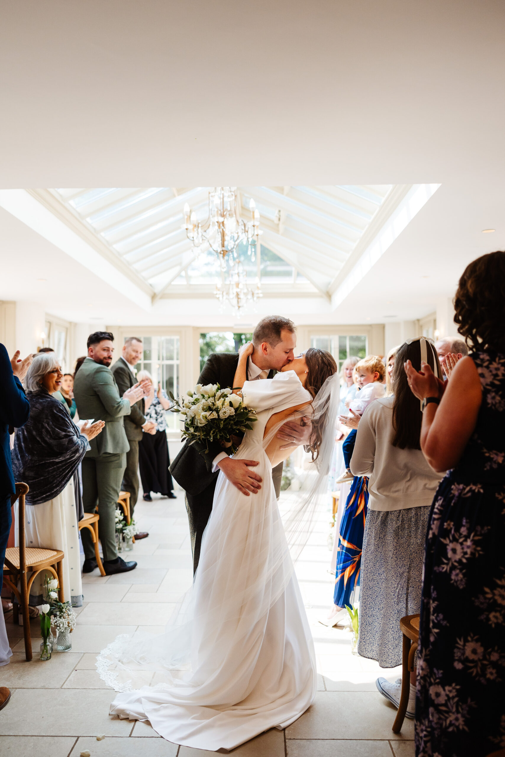 A bride and groom in the aisle of the venue embracing each other and giving each other a kiss.