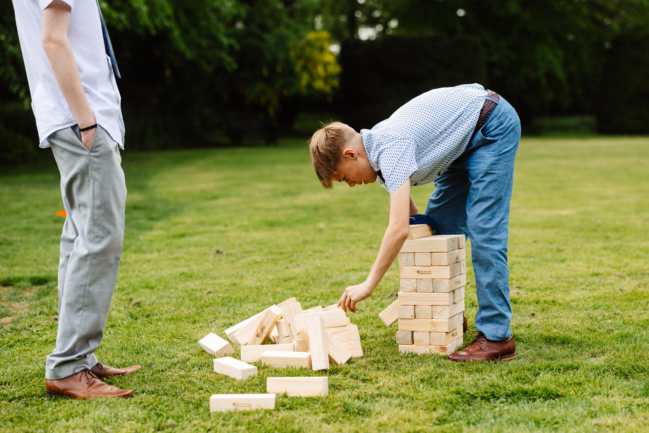 A little blue in a blue suit playing jenga in the garden of the wedding venue.