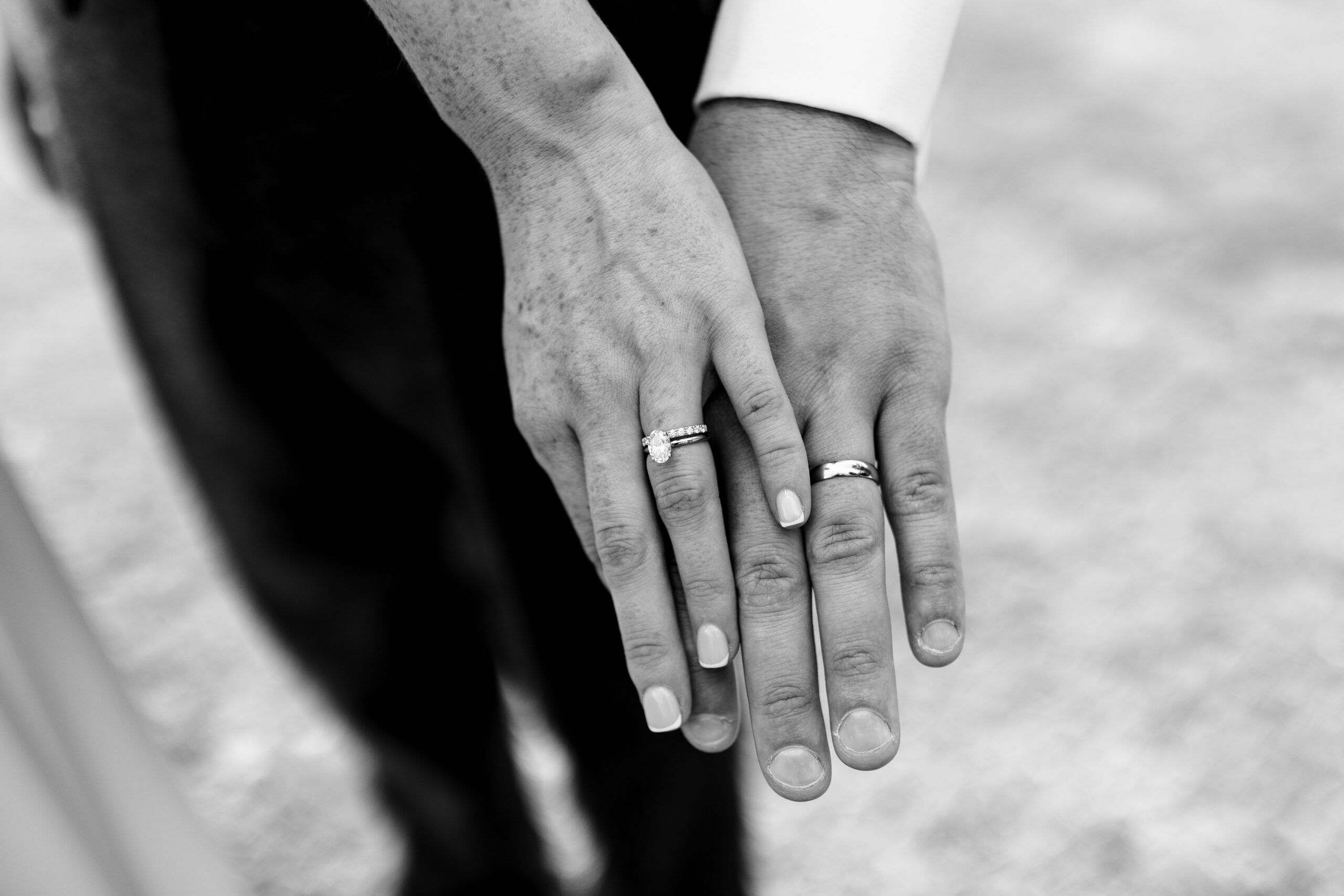 The bride and groom's hands one on top of the other showing their wedding rings. This image is black and white.