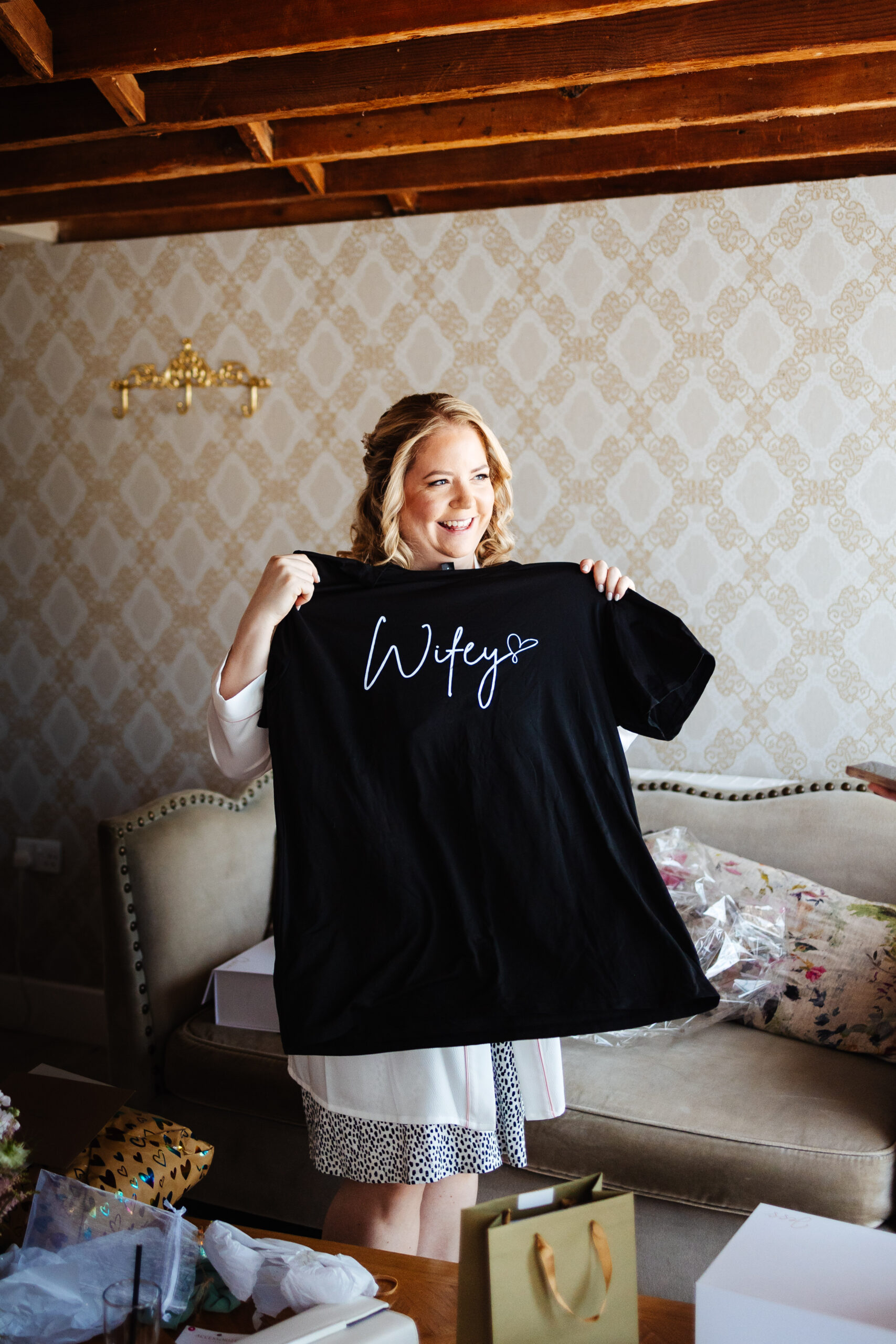 The bride holding up a black t-shirt that has white writing on that says Wifey <3 