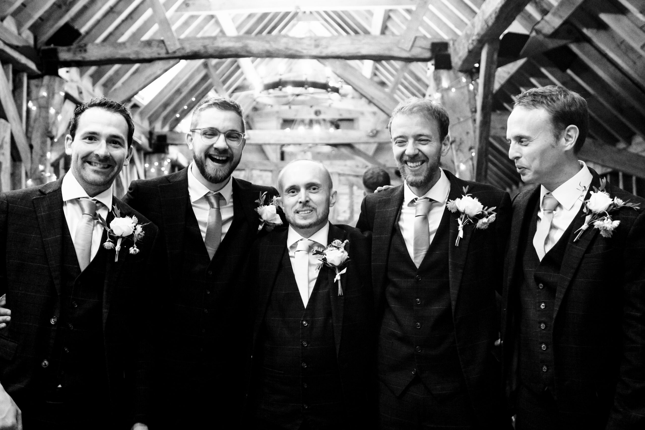 The groom and his party looking at the camera and smiling. This is minutes before he is about to get married. He looks a little nervous but the men have their arms around him in encouragement. 