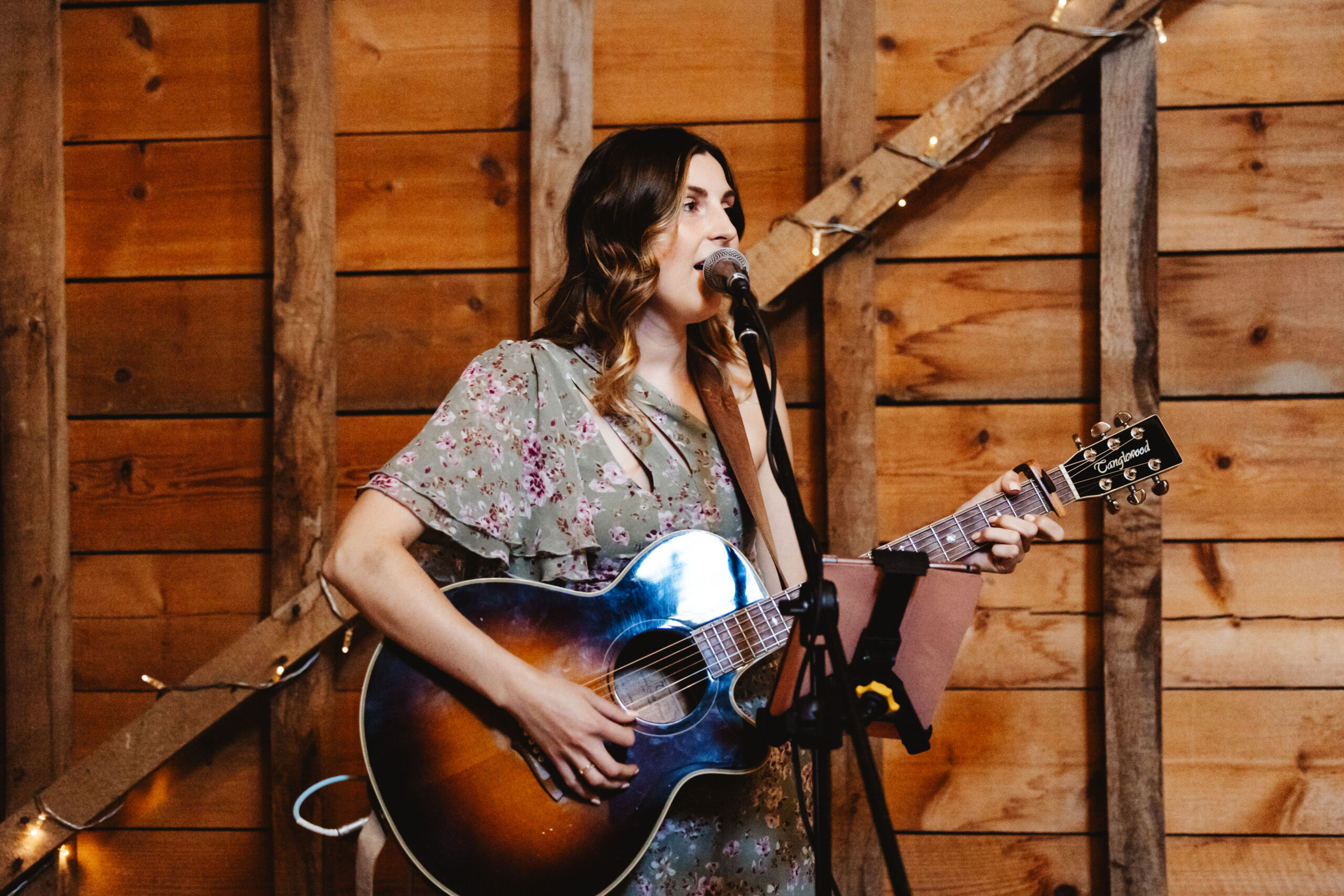 A photo of a lady with a guitar and microphone in the barn, singing.