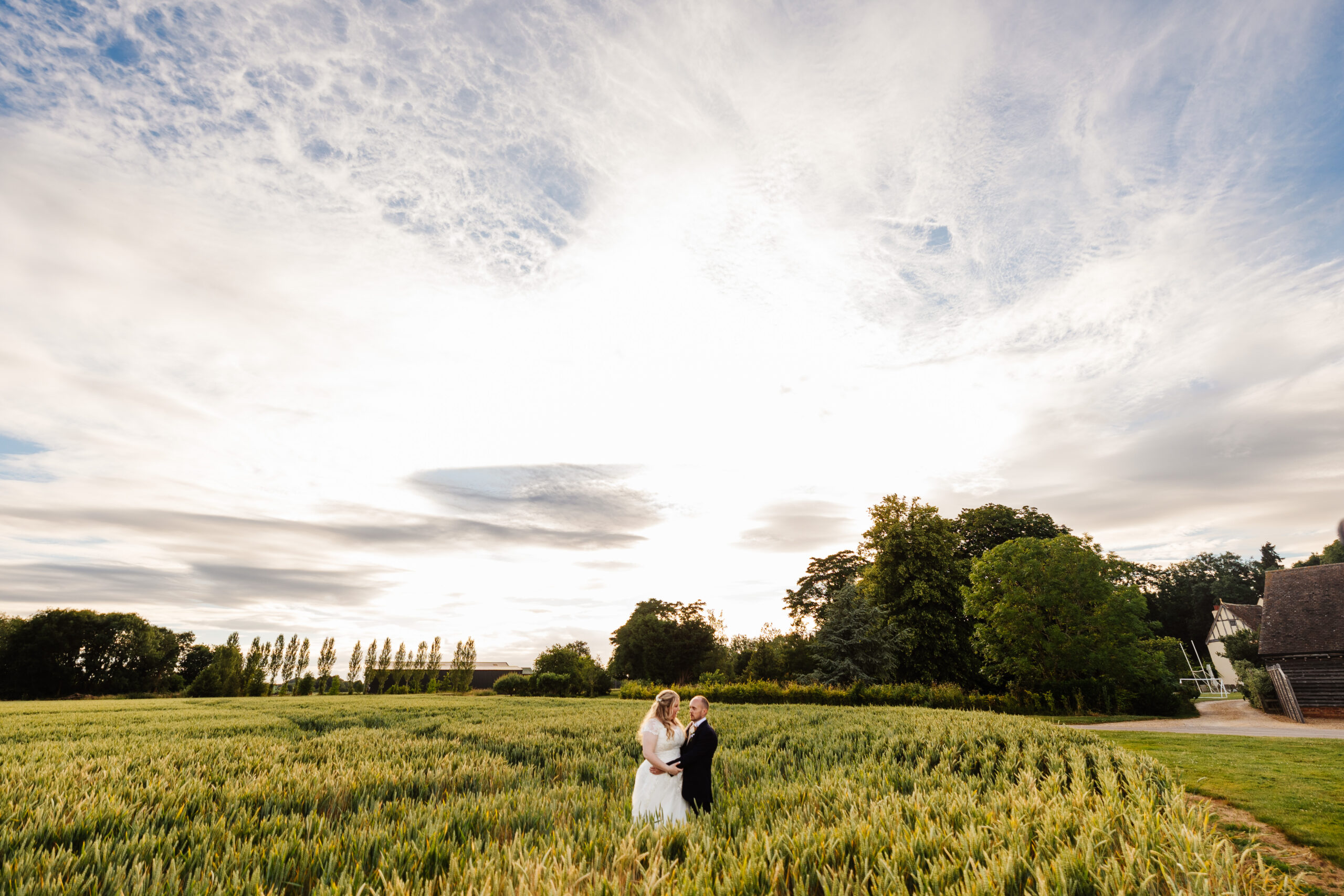 The bride and groom standing in a field. They are embracing and looking at each other.