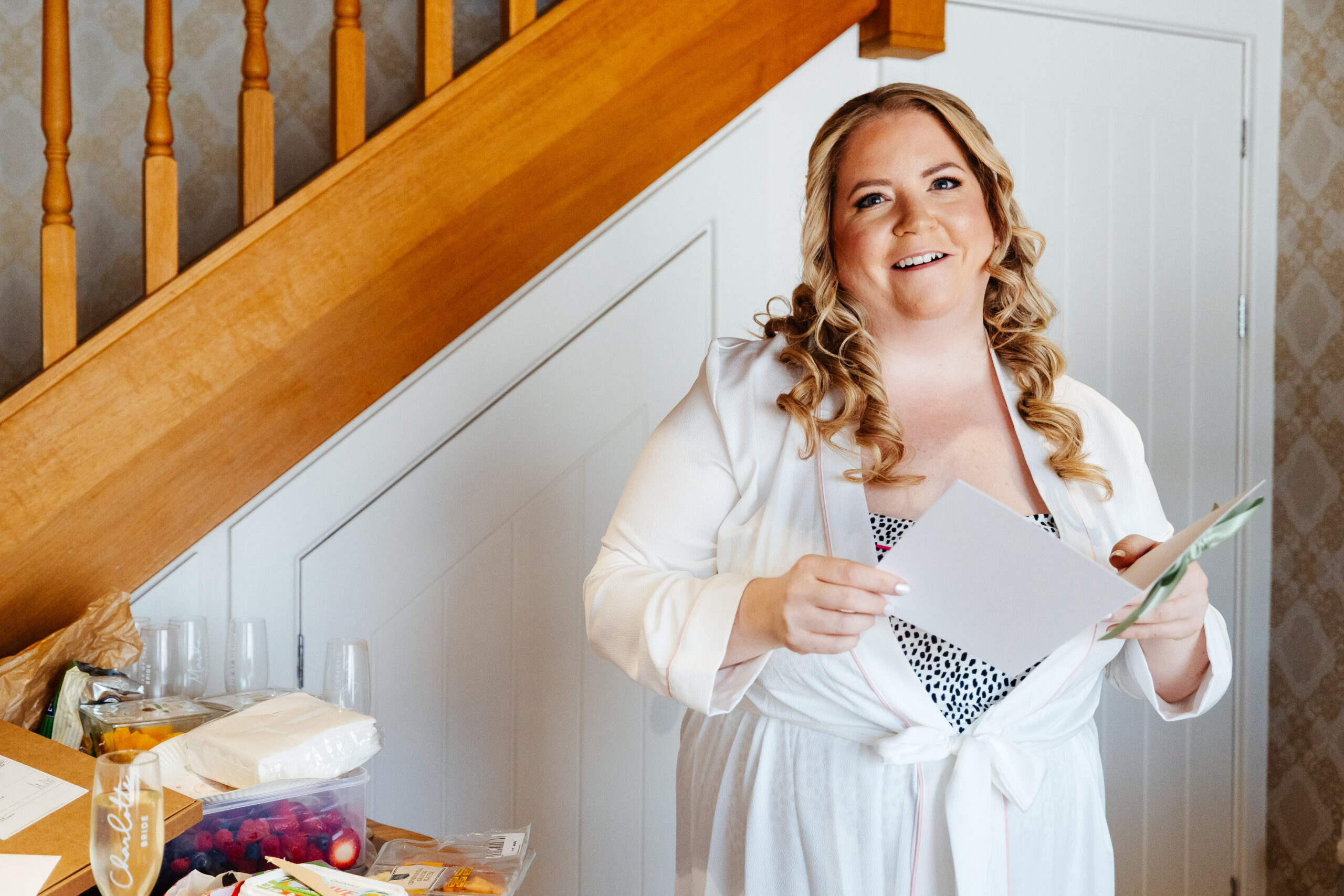 The bride reading a card from her husband. She is stood at the bottom of the stairs and has a happy face. 