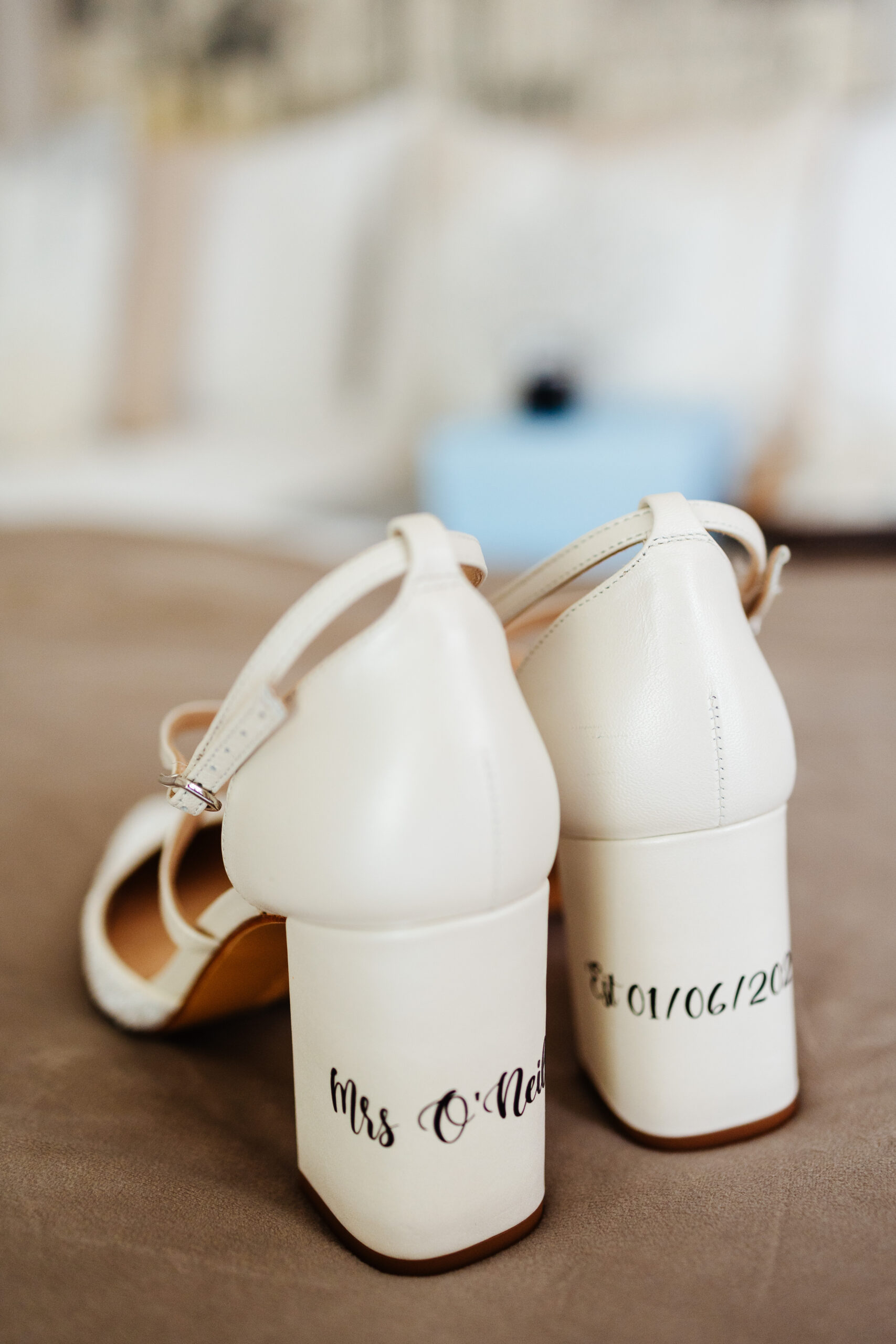 A pair of white heeled shoes. On the heel of the left shoe says "Mrs O'Neill" and the date of the wedding 01/06/2023 on the other.