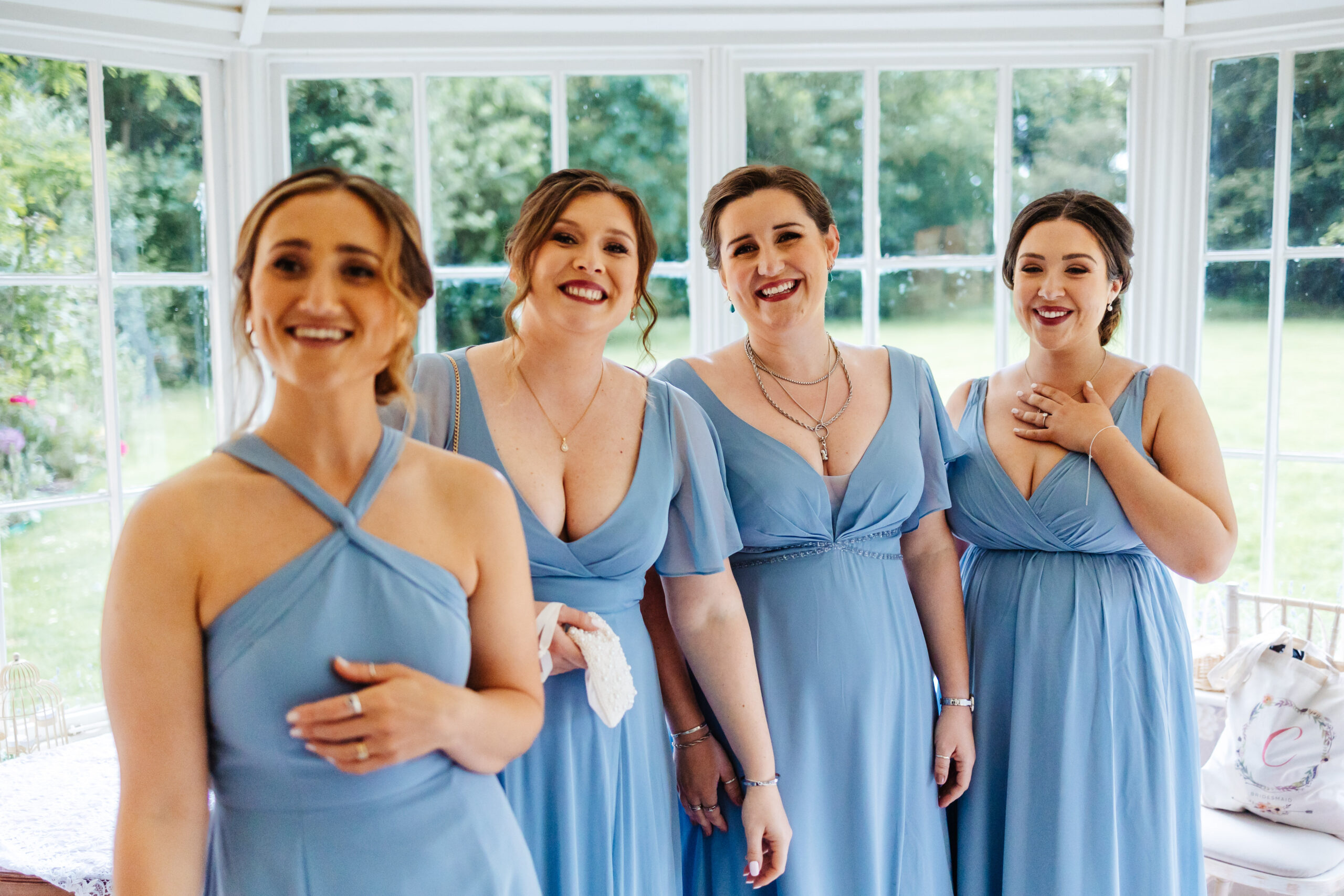 Four bridesmaids wearing pale blue dresses. All dresses are different. They are smiling and looking at the bride. You cannot see the bride, just their reactions.