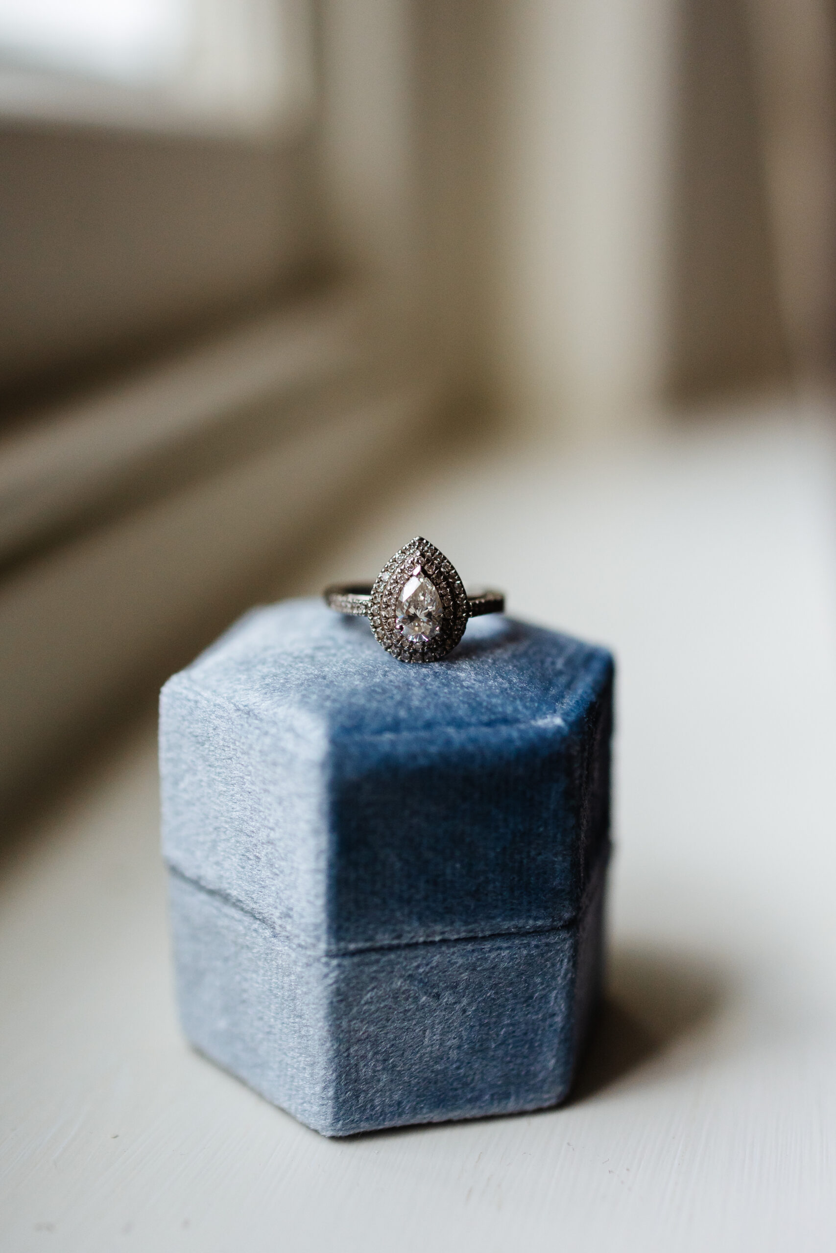 A photo of a diamond, tear drop shaped ring on top of a pale blue ring box.