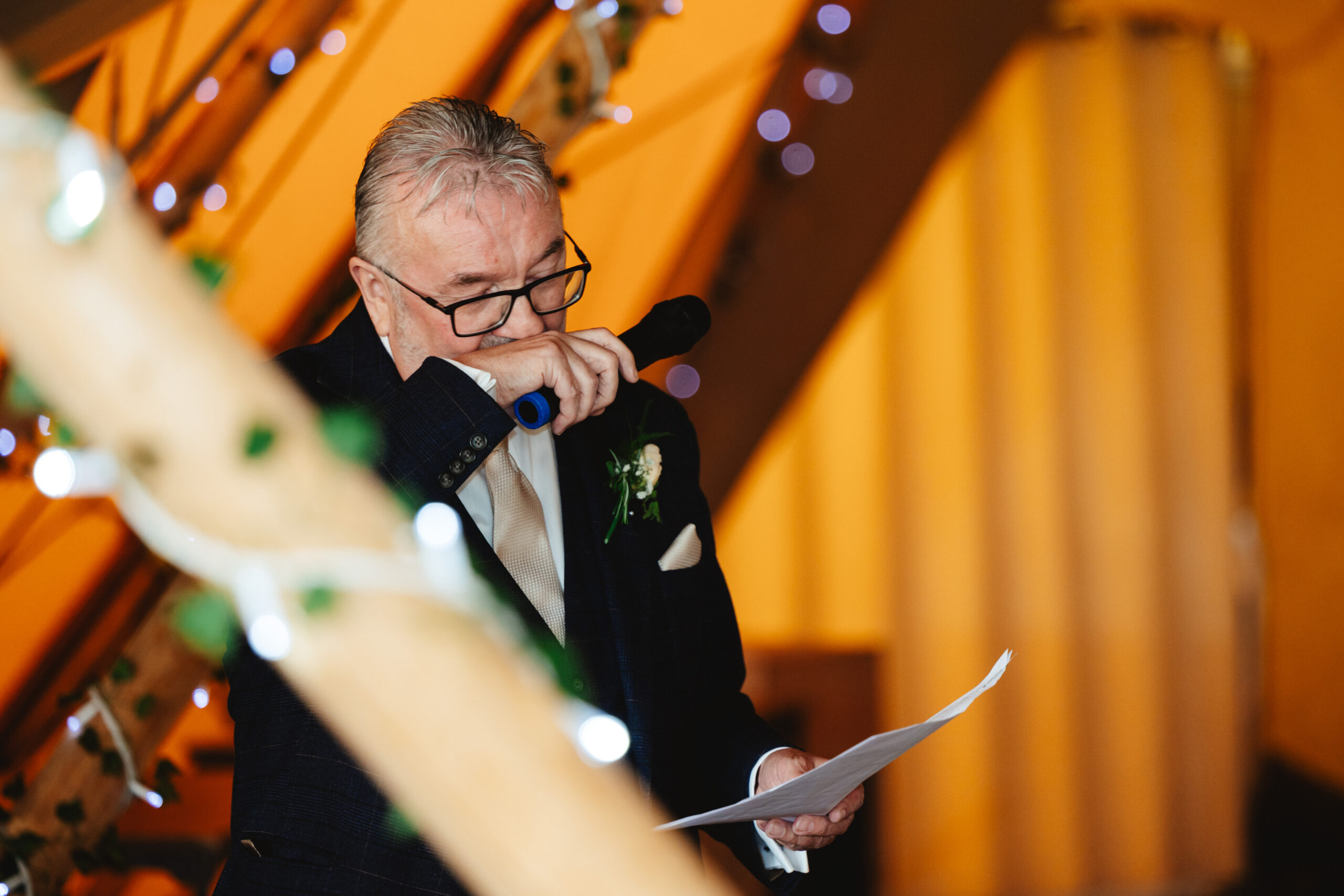 A man holding back tears. He is holding a microphone as though he is doing a speech.
