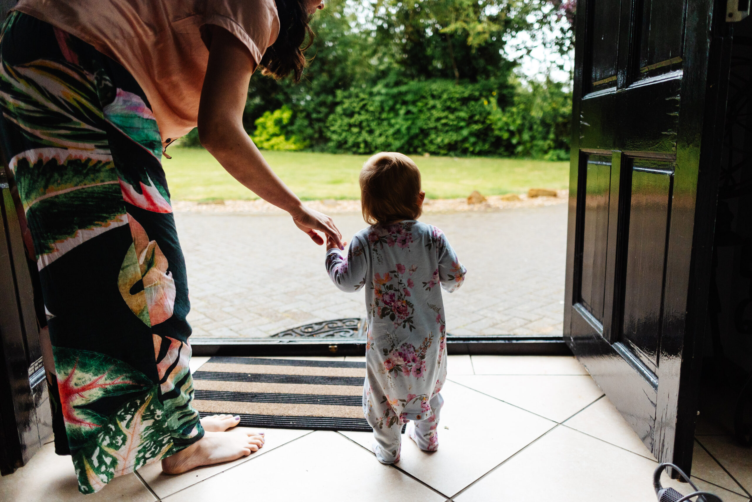 A little girl stood in a doorway holding an adults hand. They are both in pyjamas.