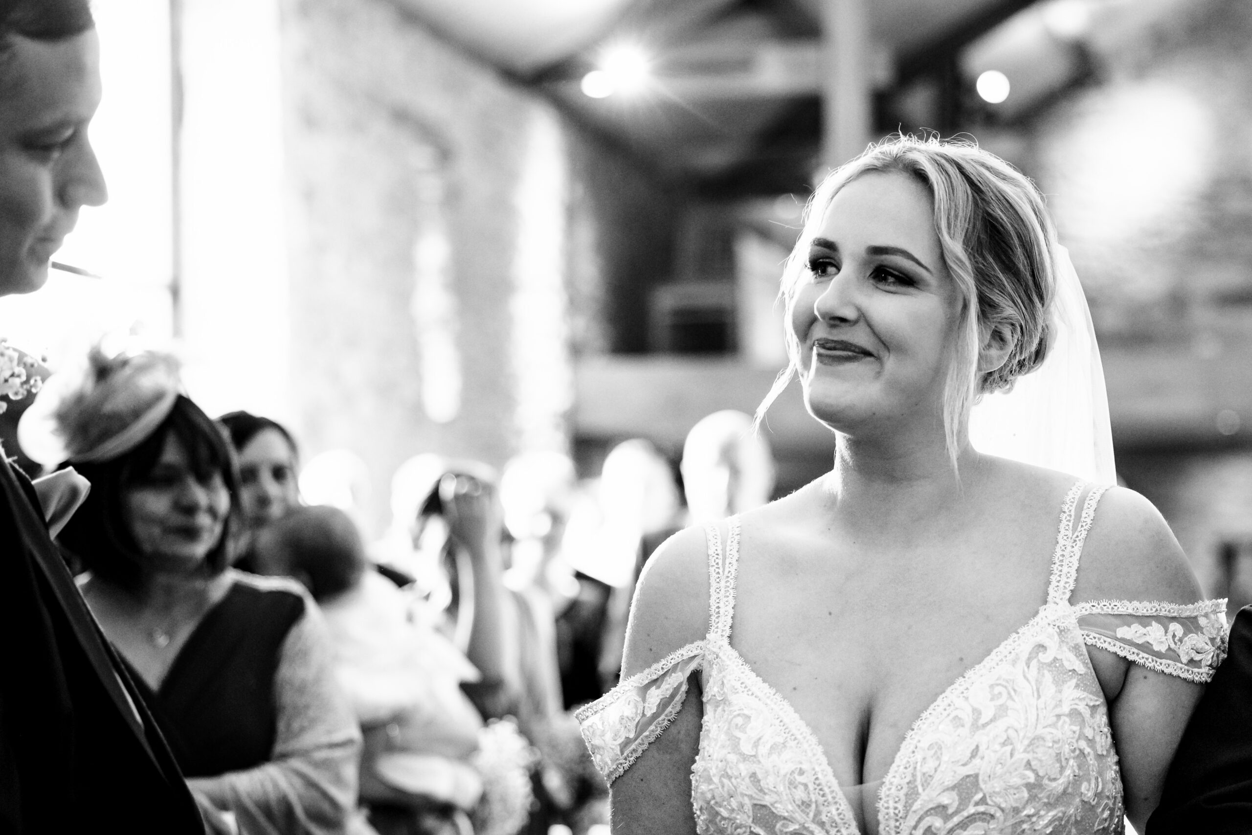 A bride looking at her groom and smiling. They are standing in the middle of the aisle.