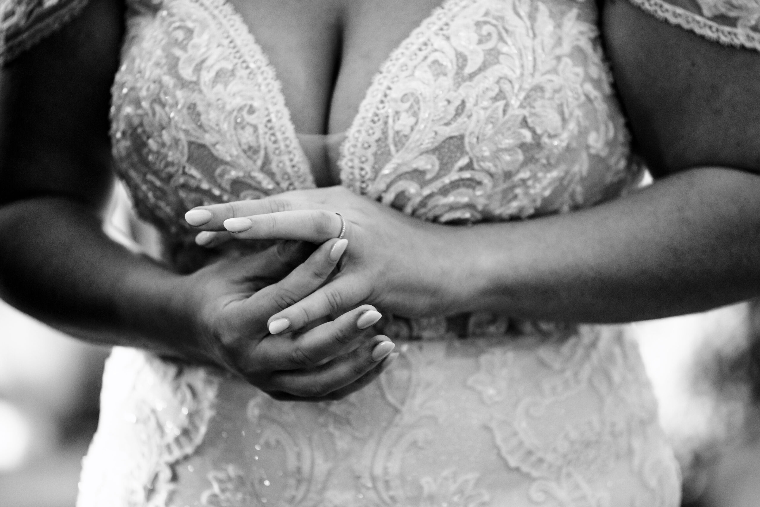 A bride's hands in front of her lace wedding dress. She is fiddling with her new wedding ring.