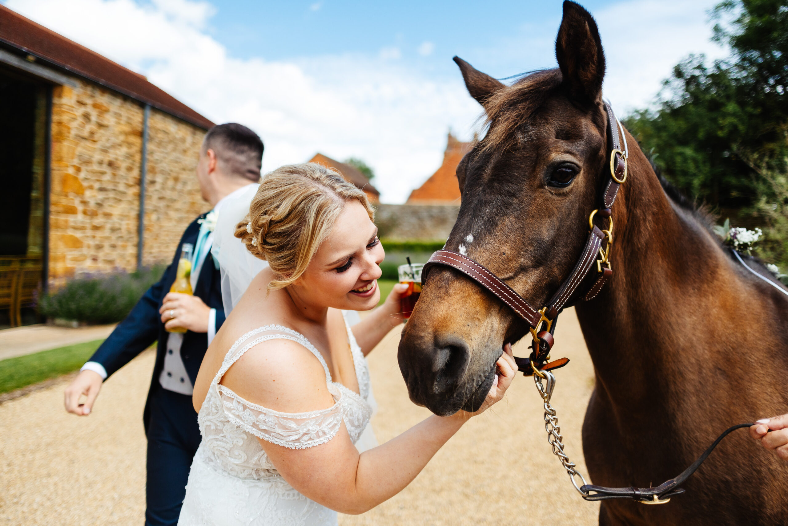 A bride standing outside looking at and smiling at her horse. The horse is brown and has a leather strap around its face. 