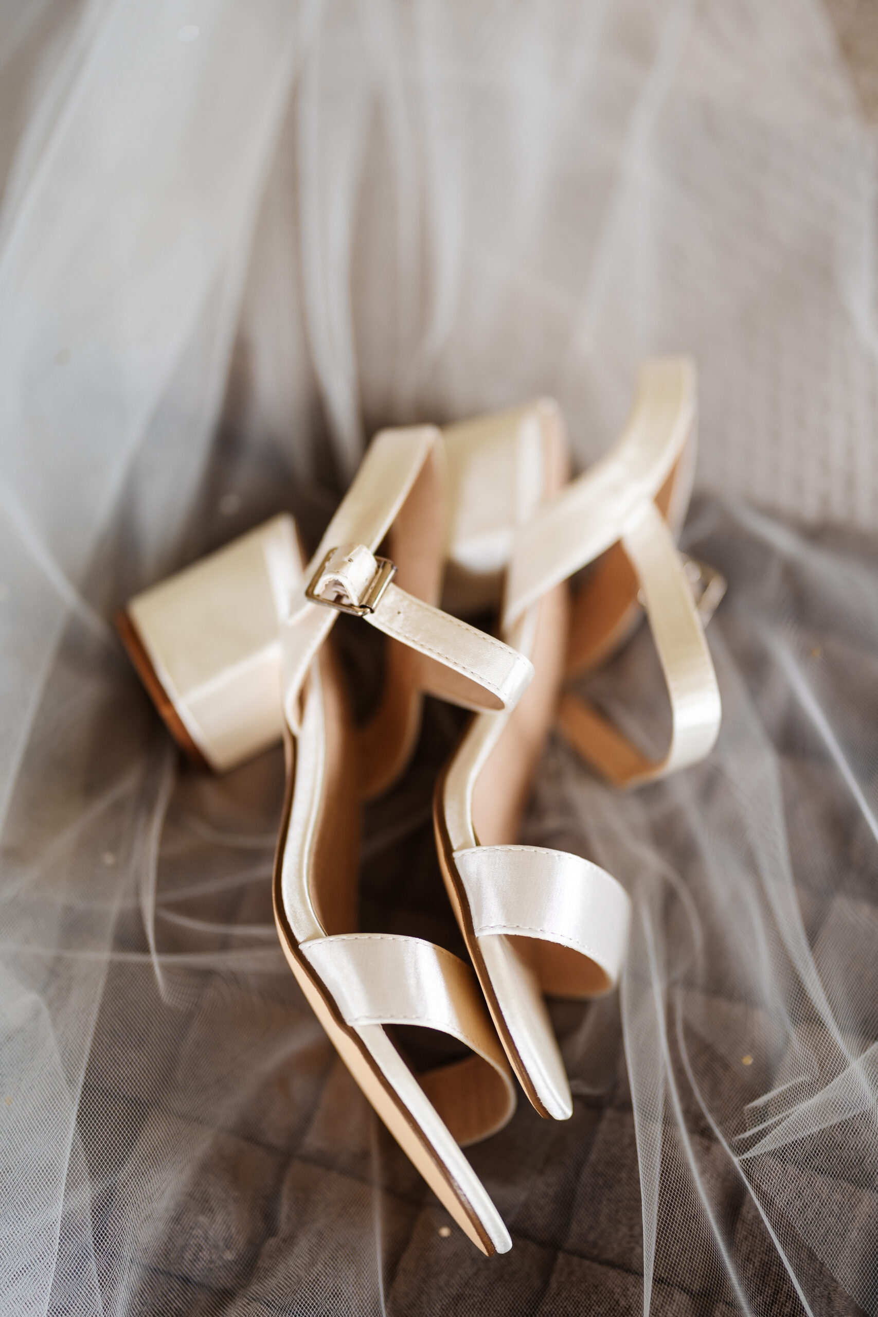 A pair of white, satin heels on top of a see through white veil.