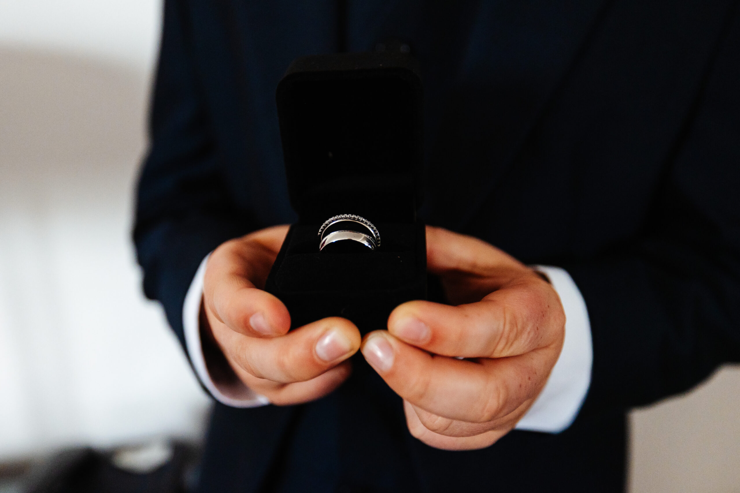 A black box containing two silver rings in held in a pair of hands.