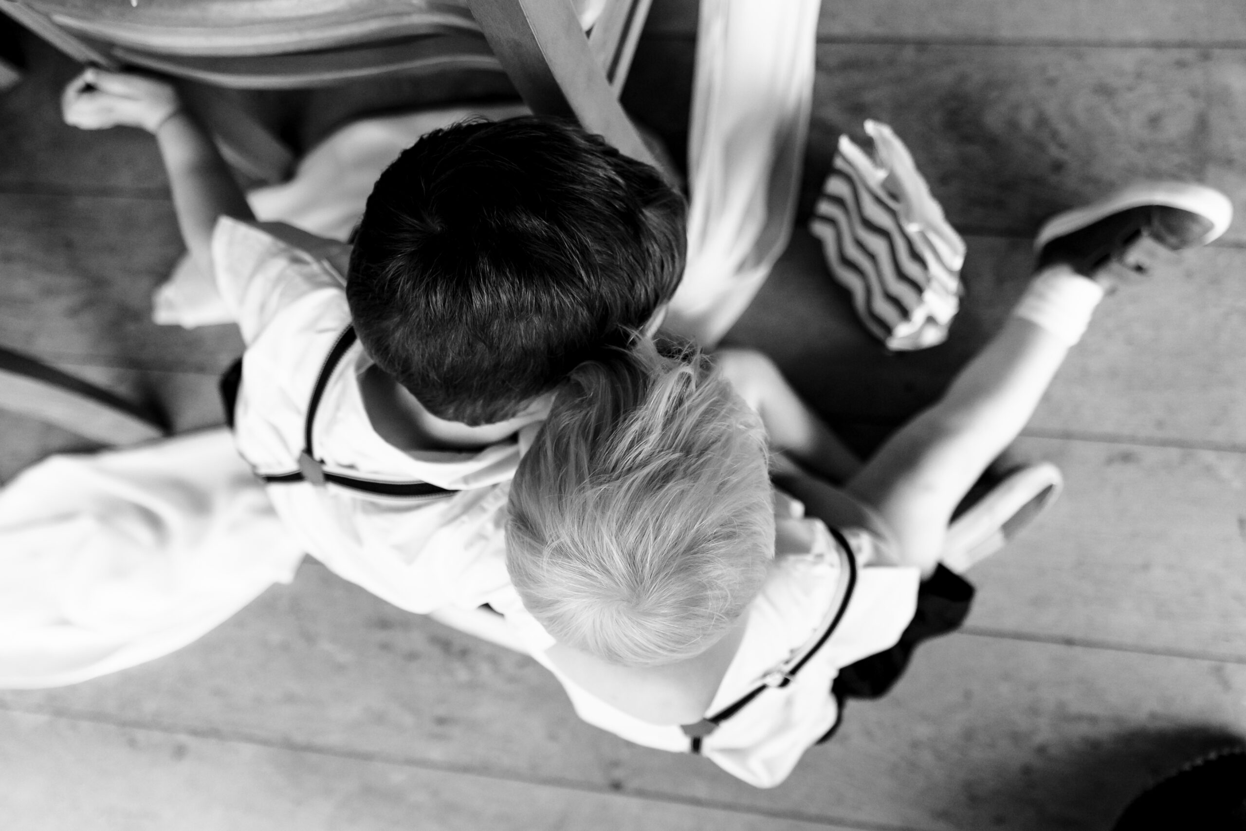 A black and white photo of two boys sat down on the floor. You can see the top of their heads - they are in white shirts and braces.