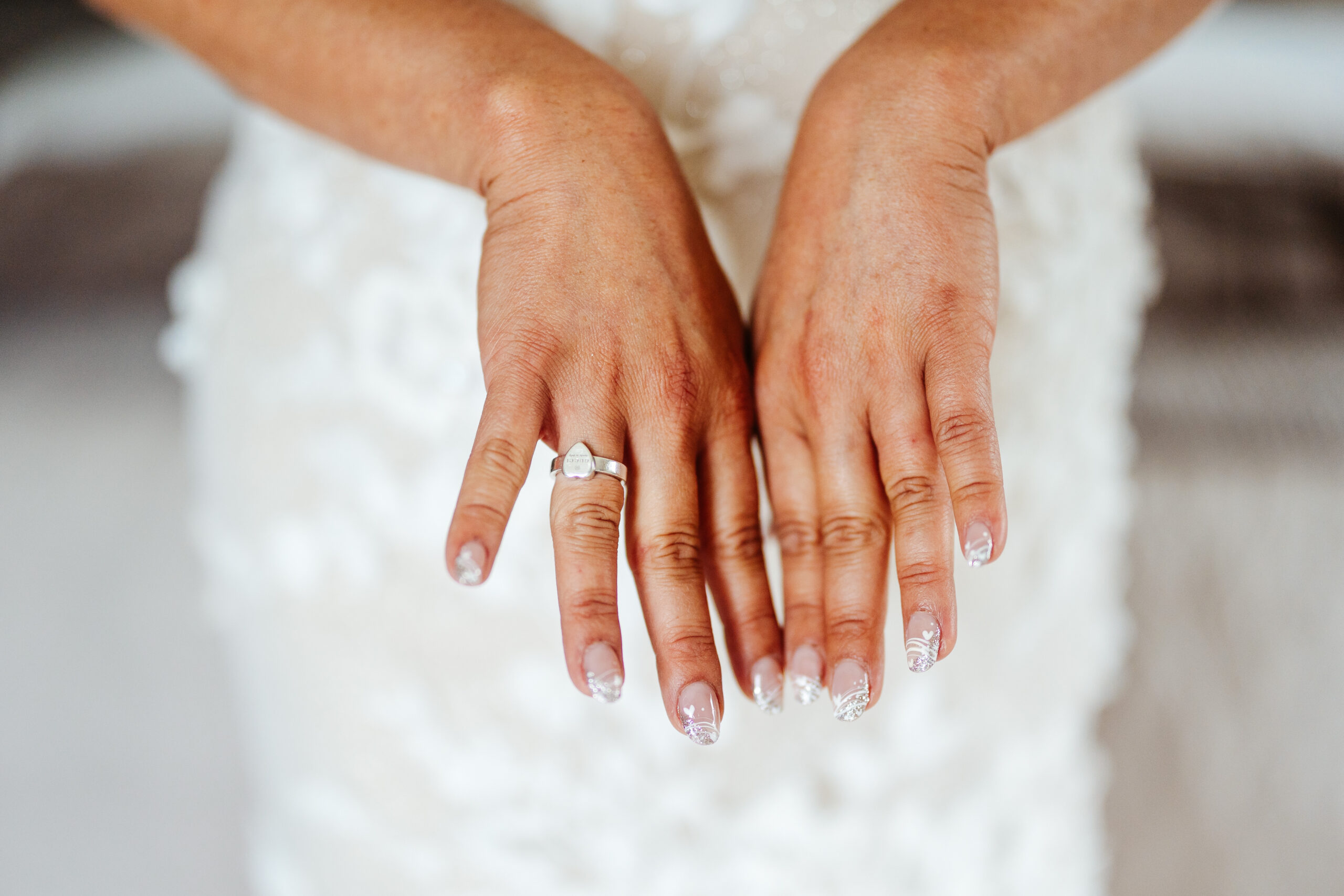 A photo of the brides hands. She has a heart shaped ring on her ring finger and her nails have white heart details on them.