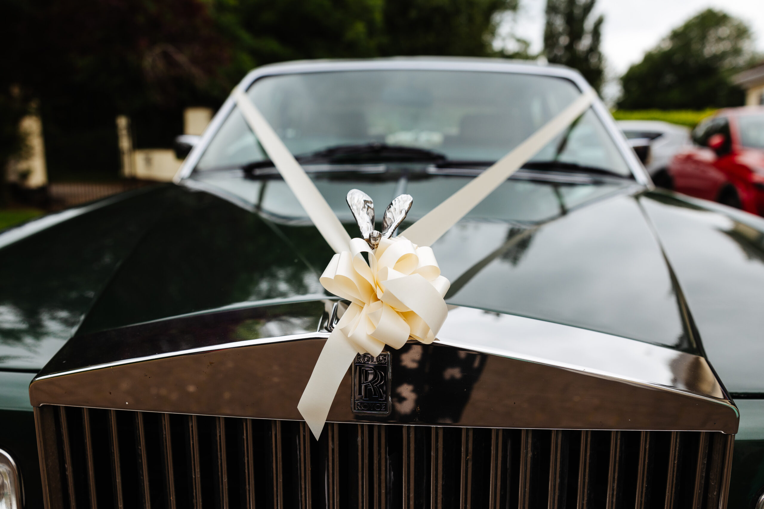 An image of a black, wedding car with a white/cream ribbon dressing it in true, traditional style.