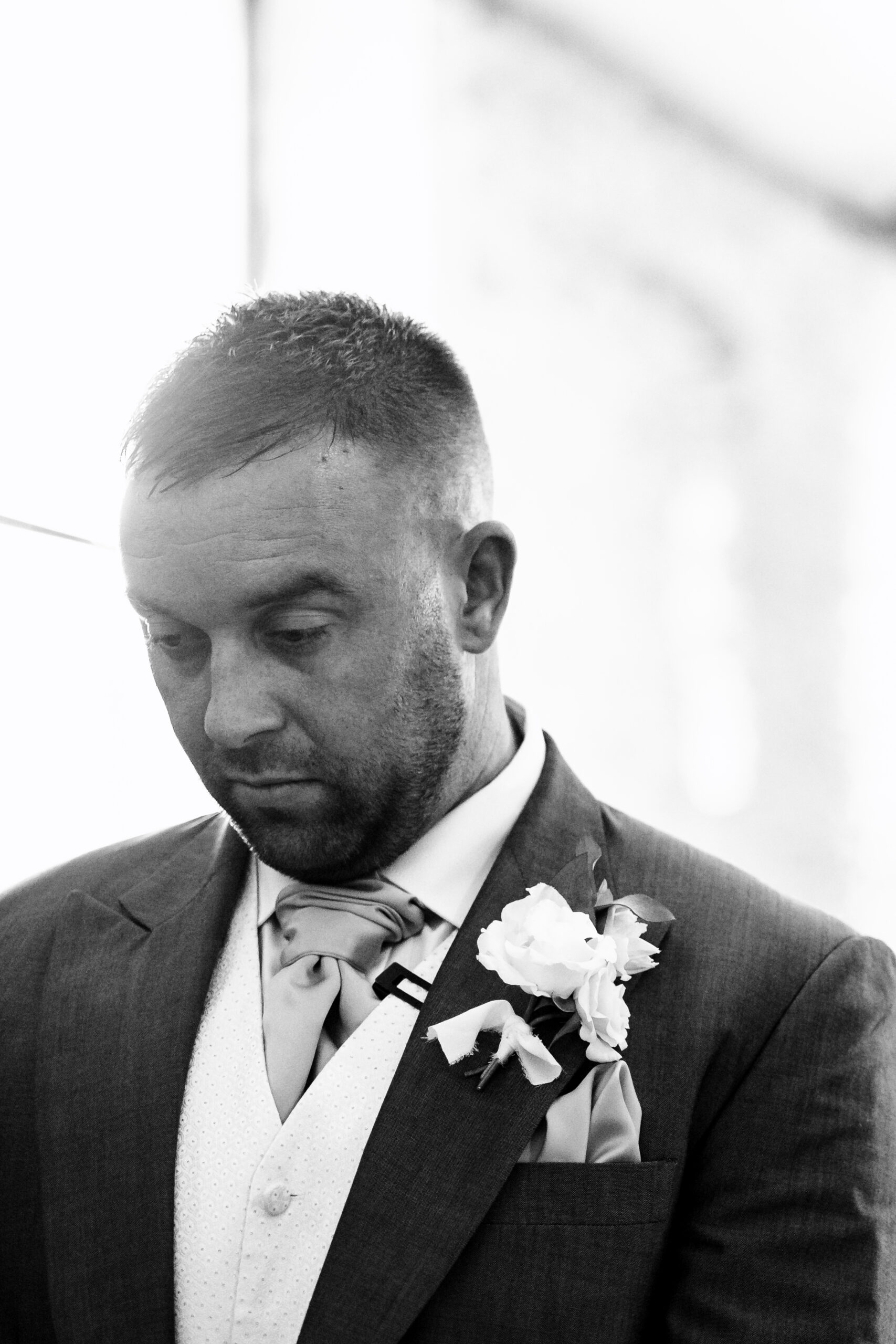 A black and white photo of a groom. Her is looking down and is nervous. 