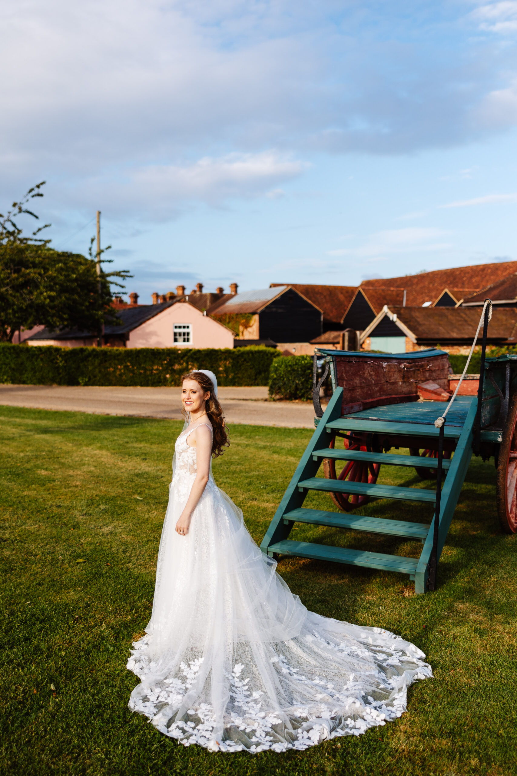 The bride is in the garden on her own. Her dress is spread around her and you can see all of the detail of the lace clearly. She is looking away from the camera, smiling.